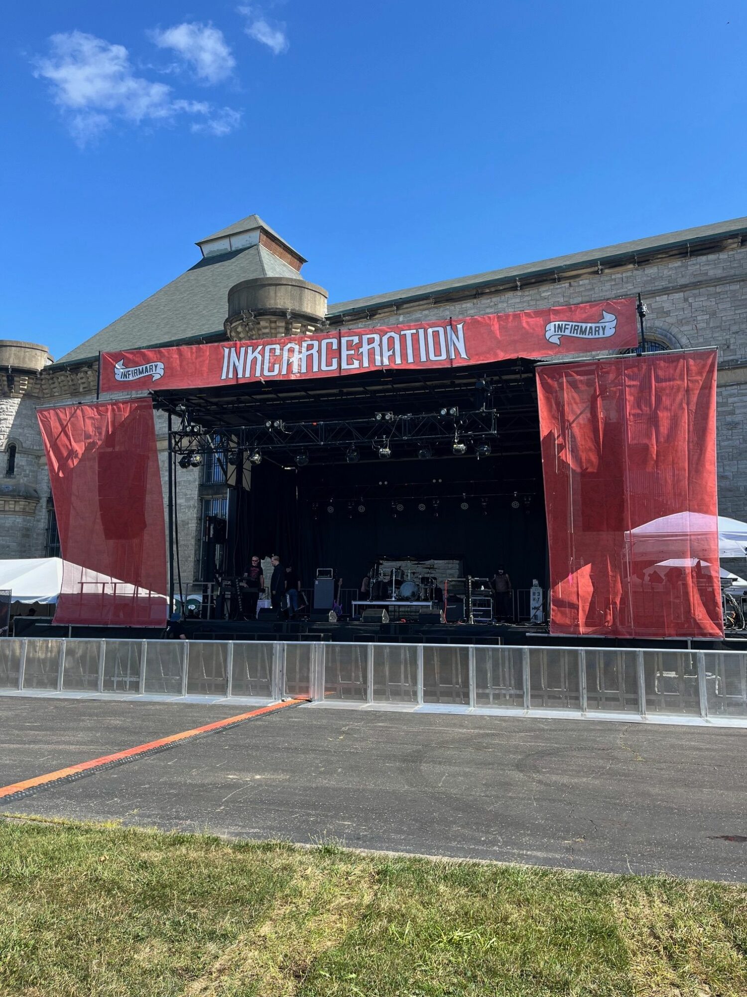 Empty outdoor stage with red curtains and a banner reading 'INCARCERATION' under a blue sky.