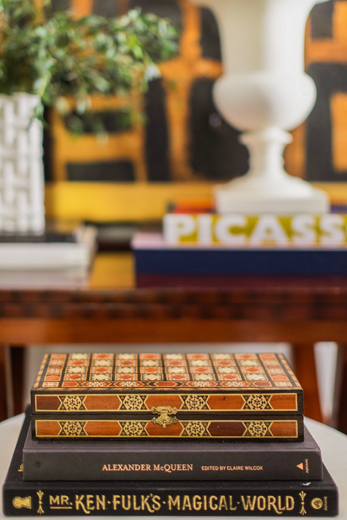 Stacked decorative boxes on a wooden table with books and a white lamp in background.