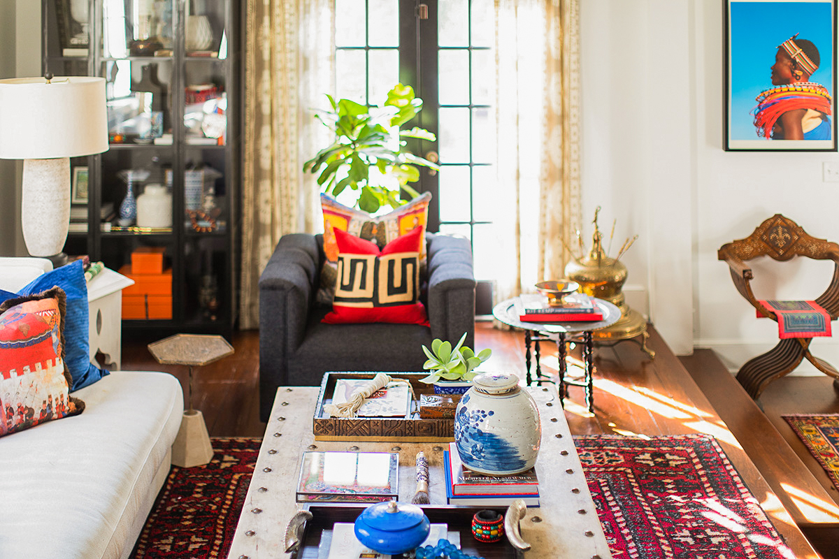 Living room with sofa, armchair, coffee table, and decorative items, sunlight streaming through windows, and artwork on wall.
