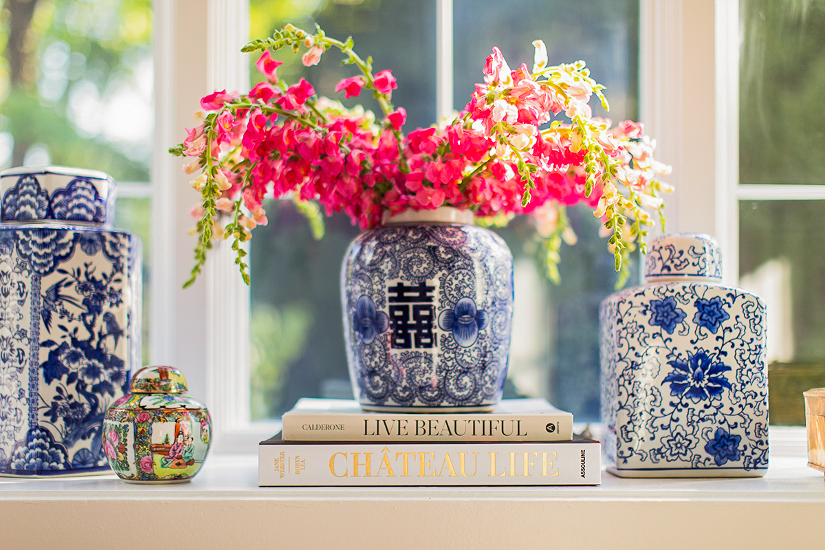 Flower arrangement in a blue and white vase on a windowsill with books and decorative objects.