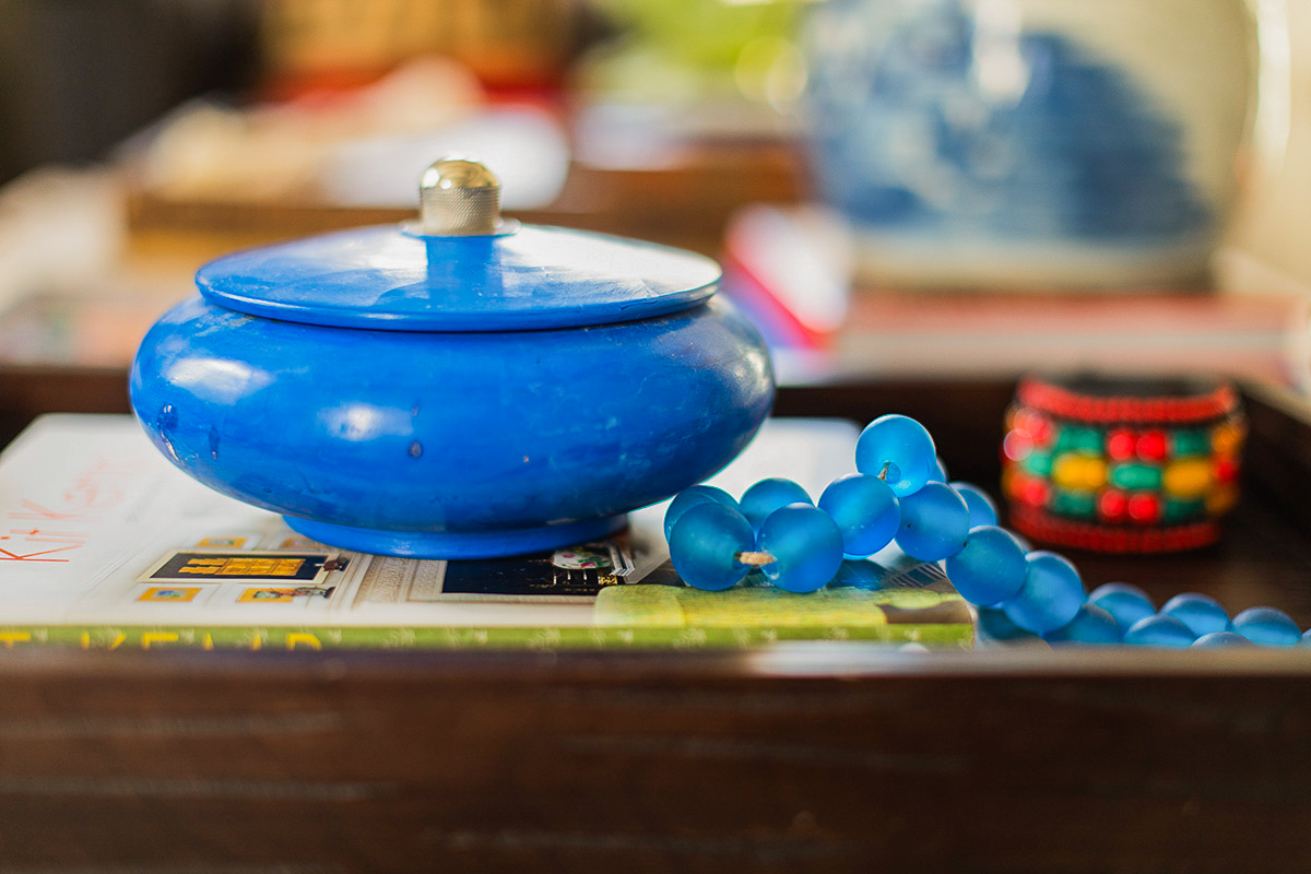 Blue container with a lid, small blue beads, and a colorful beaded bracelet on a surface with a blurred background.