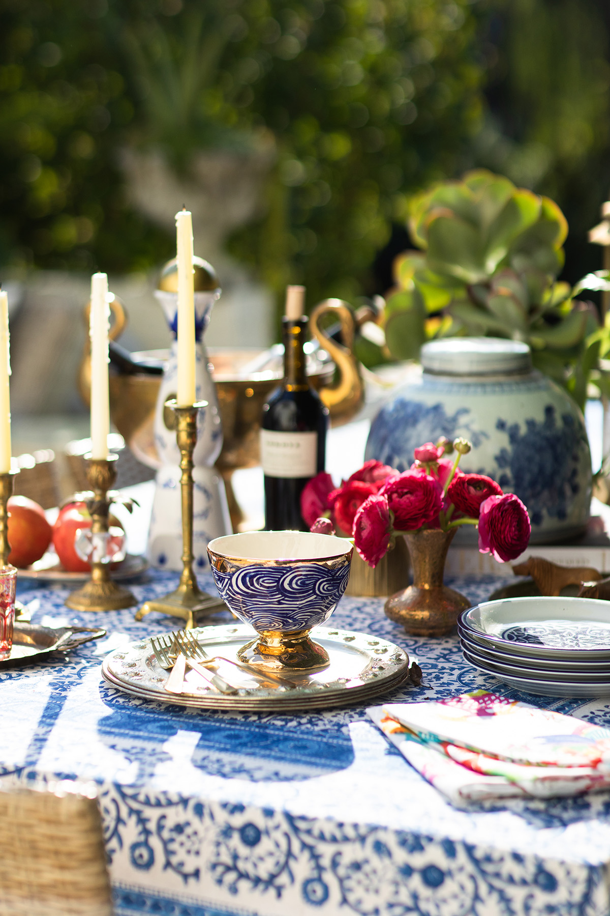 Table set with candles, flowers, plates, and a large blue and white vase outdoors.