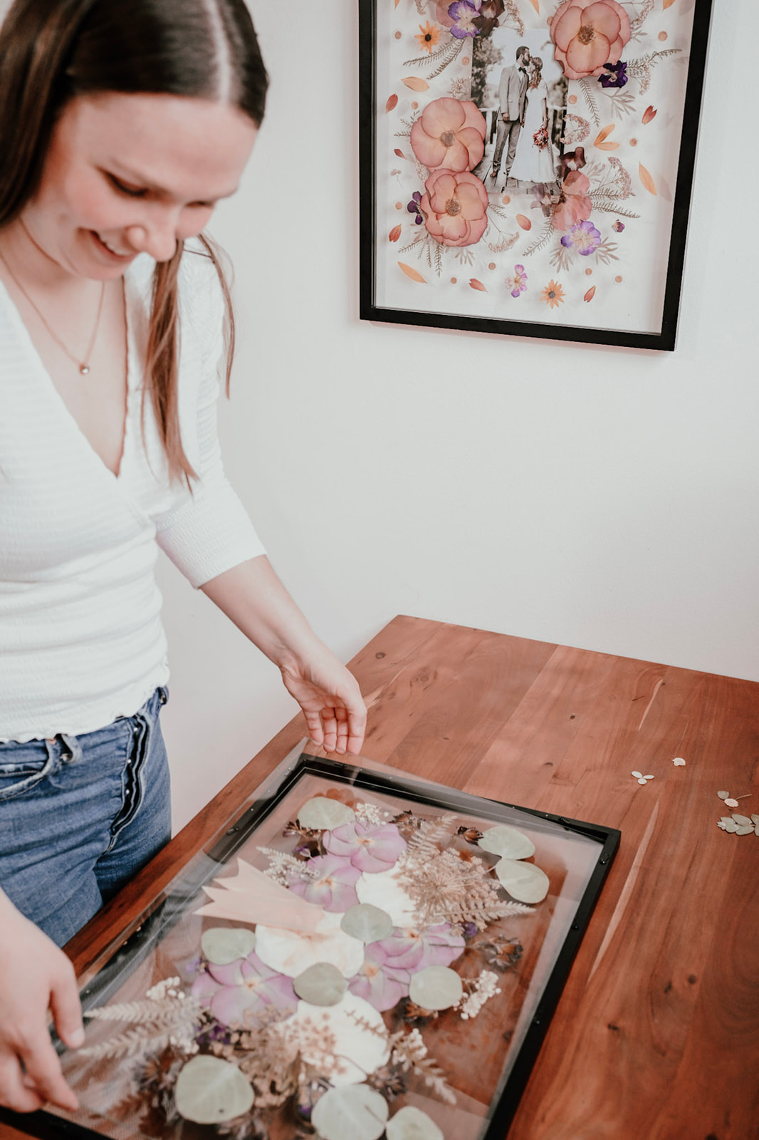Woman looking at a tray with various decorated cookies on a wooden table, with framed artwork on the wall behind.
