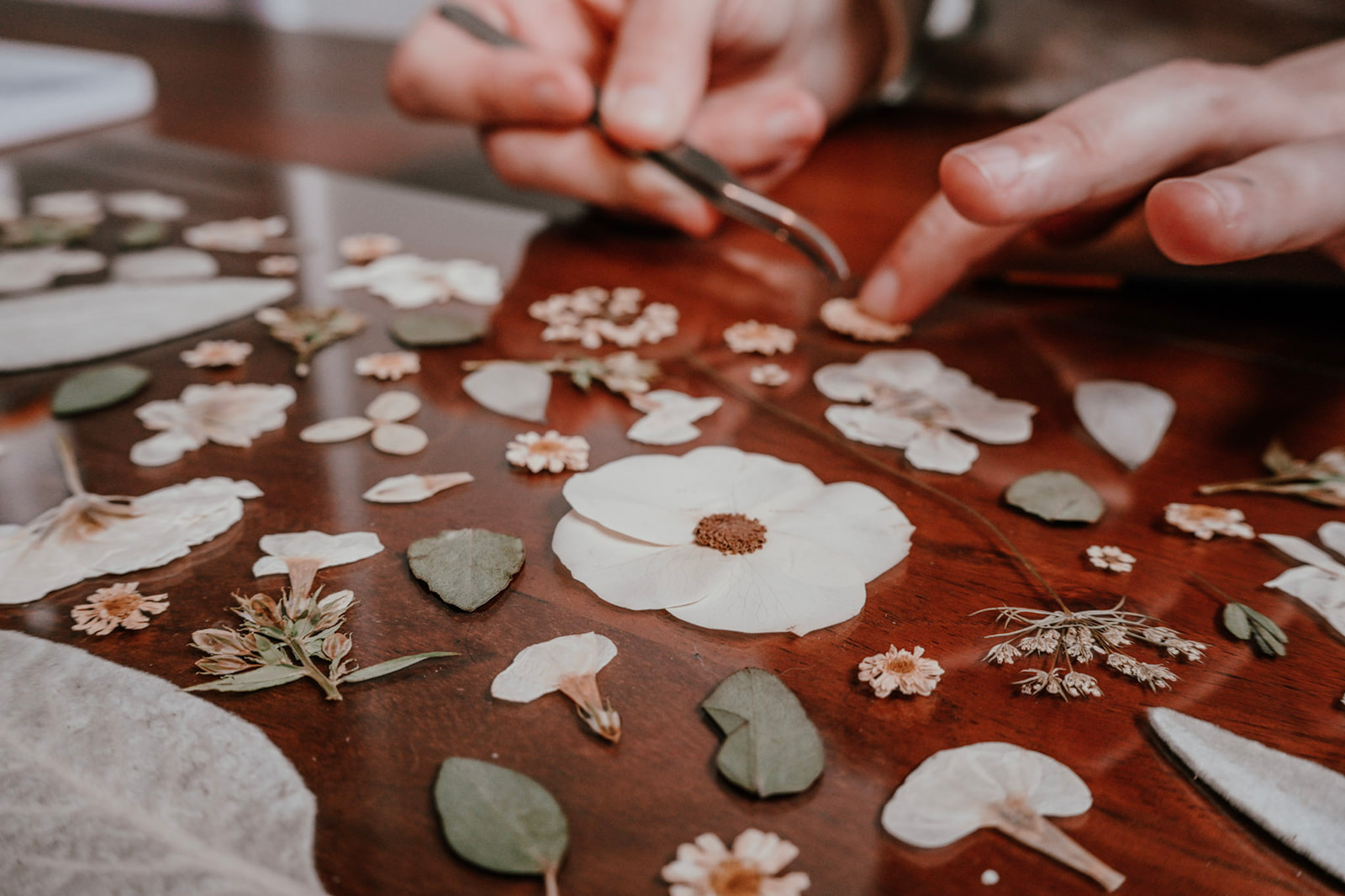 Hands arranging small flower-shaped and leaf-shaped paper cutouts on a wooden surface.
