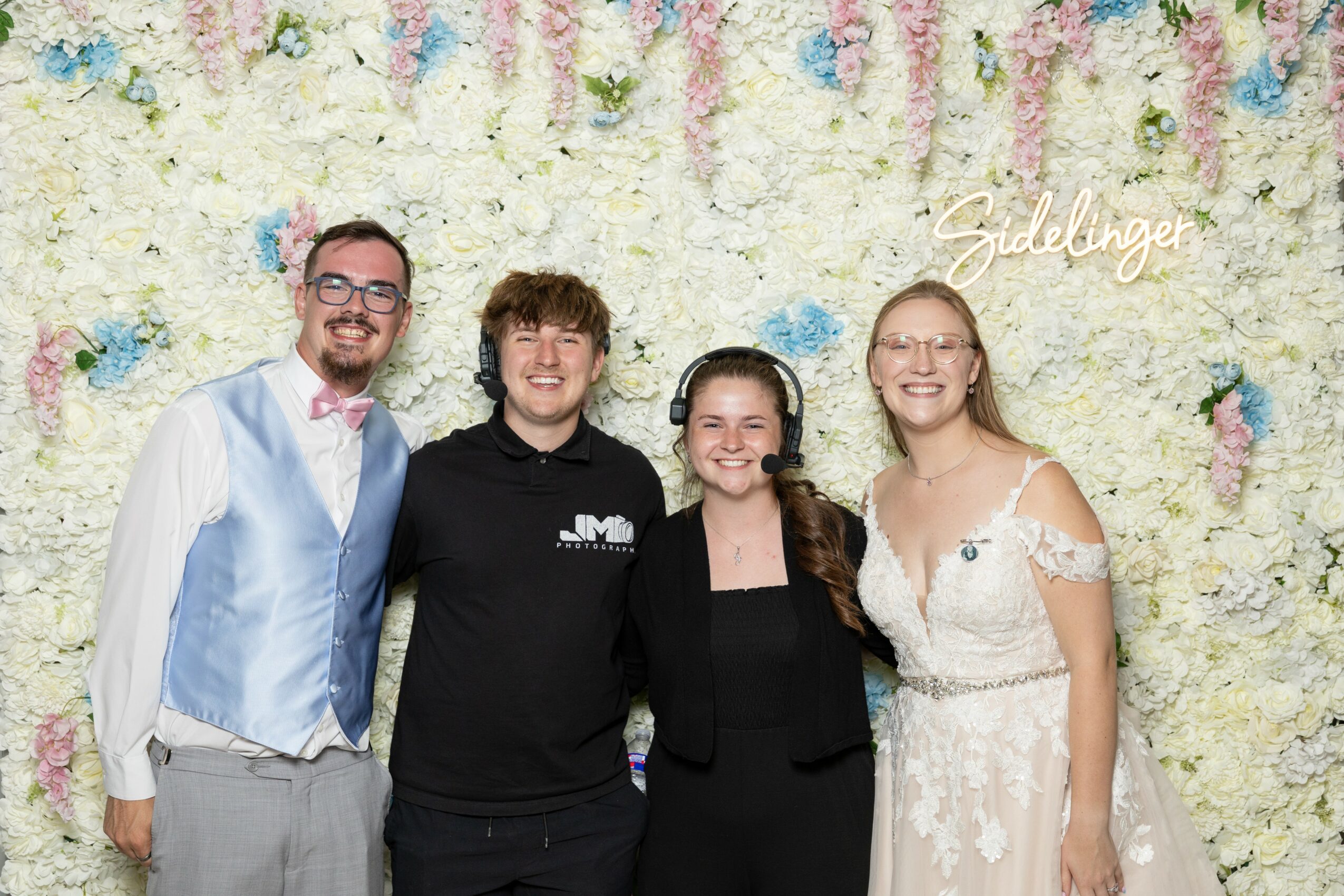 Four people standing in front of a floral backdrop, smiling, with a sign that says 'Geldange'.