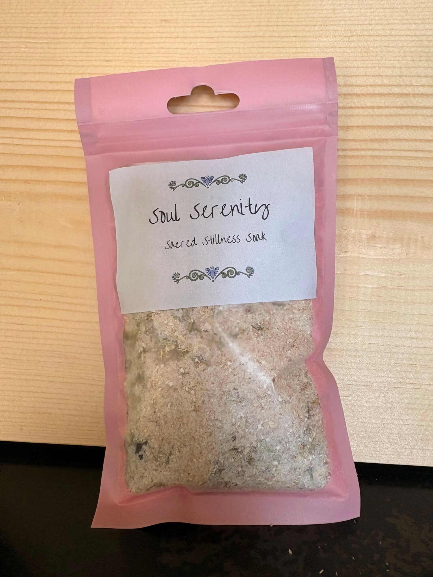 Pink resealable bag labeled 'Soul Serenity' with herbal salt inside, placed on a wooden surface.