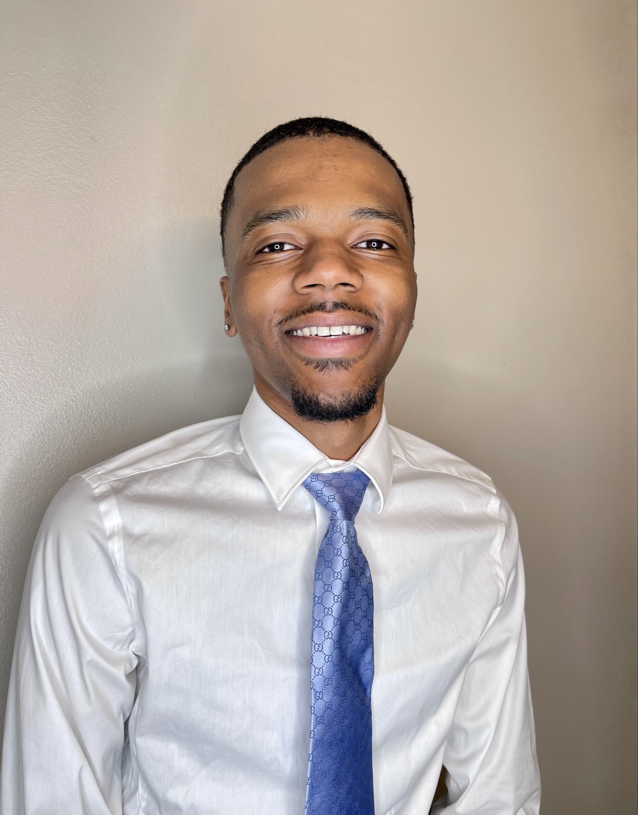 Smiling man in white shirt and blue tie against plain background.