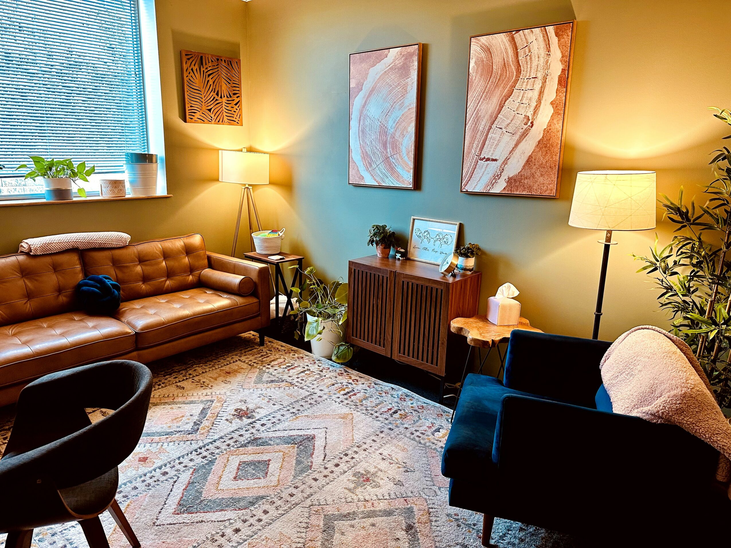 Living room with a leather sofa, armchair, paintings, lamps, and a patterned rug.