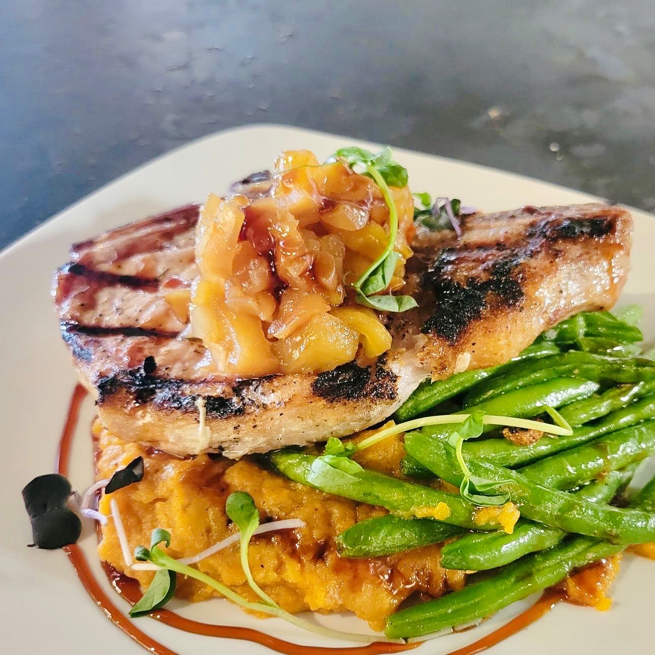 Grilled fish fillet topped with fruit salsa, served with green beans and mashed vegetables on a white plate.