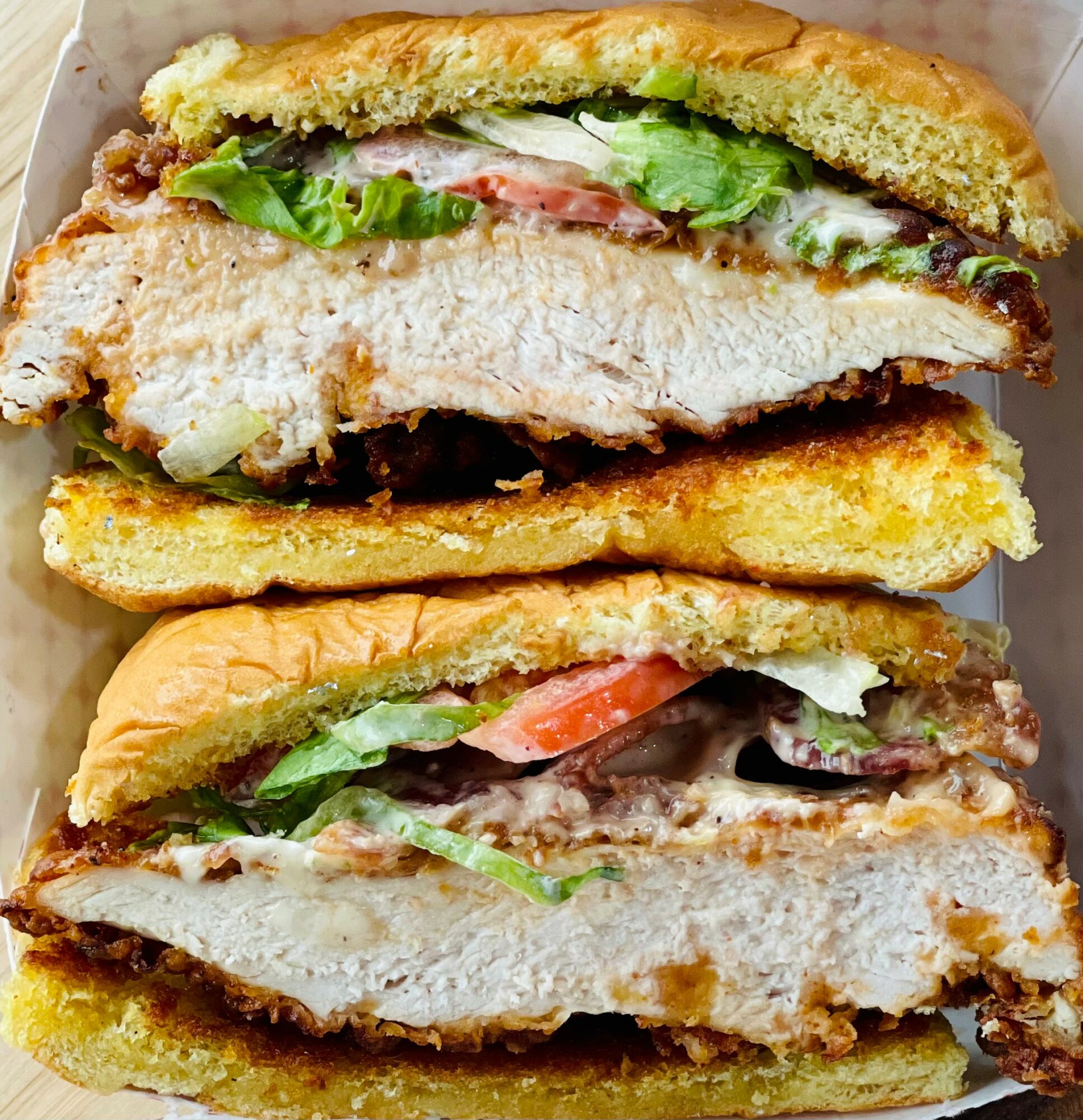 Close-up of a sandwich with fried chicken, lettuce, tomato, and sauce in a toasted bun.