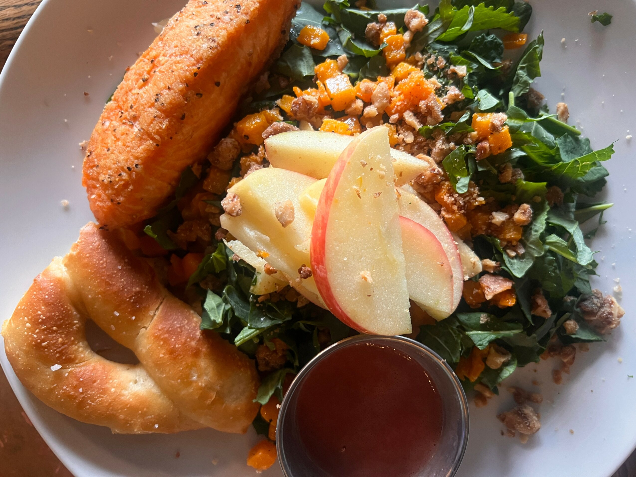 Salad with apple slices, greens, chopped vegetables, fried item, breaded item, and a small container of dressing on a white plate.