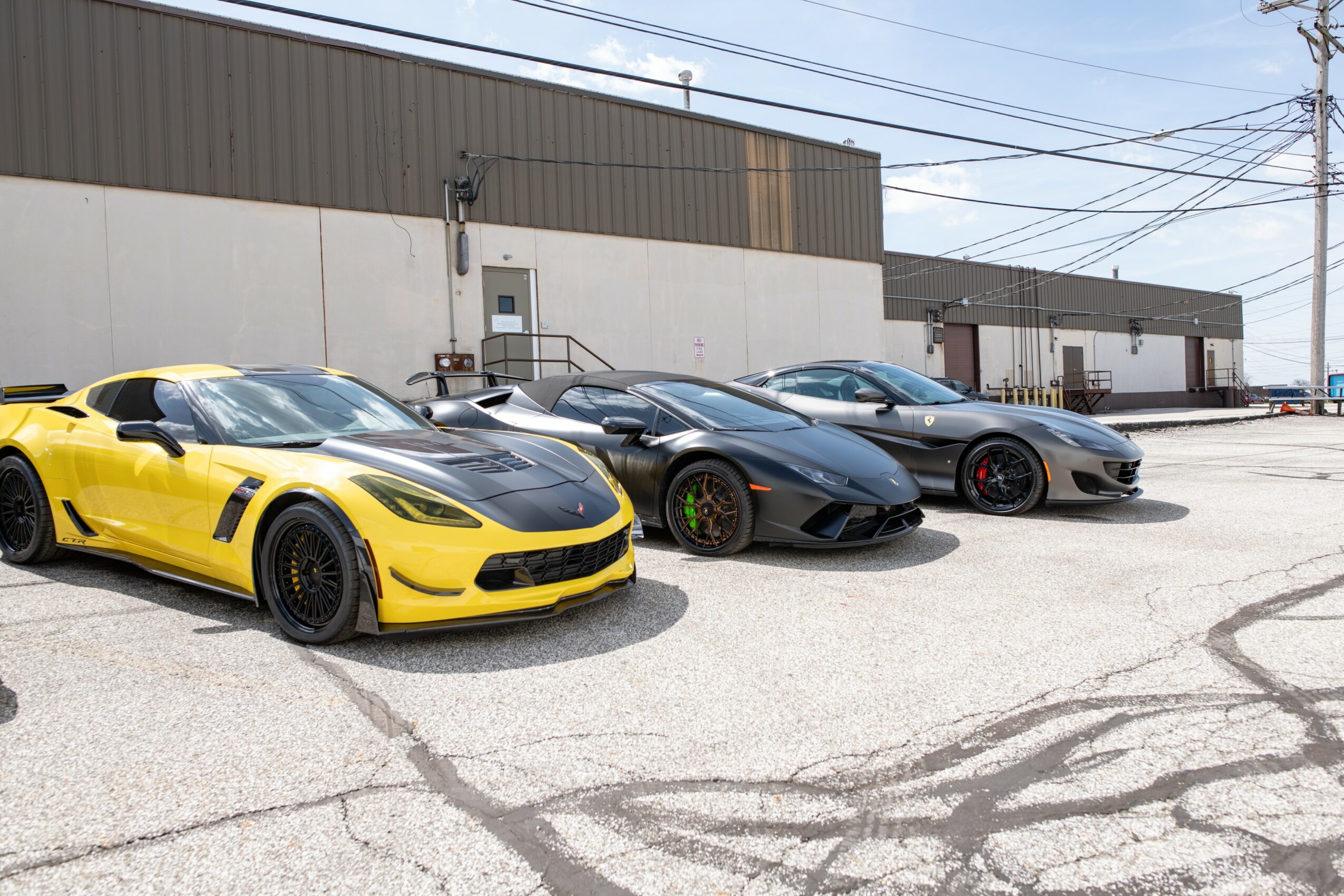 Four sports cars parked in a lot with a building and power lines in background.