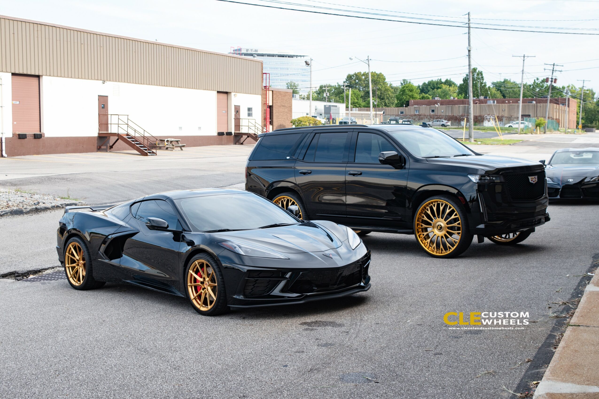 Black sports car with gold wheels parked next to a black SUV with gold wheels in a parking lot.
