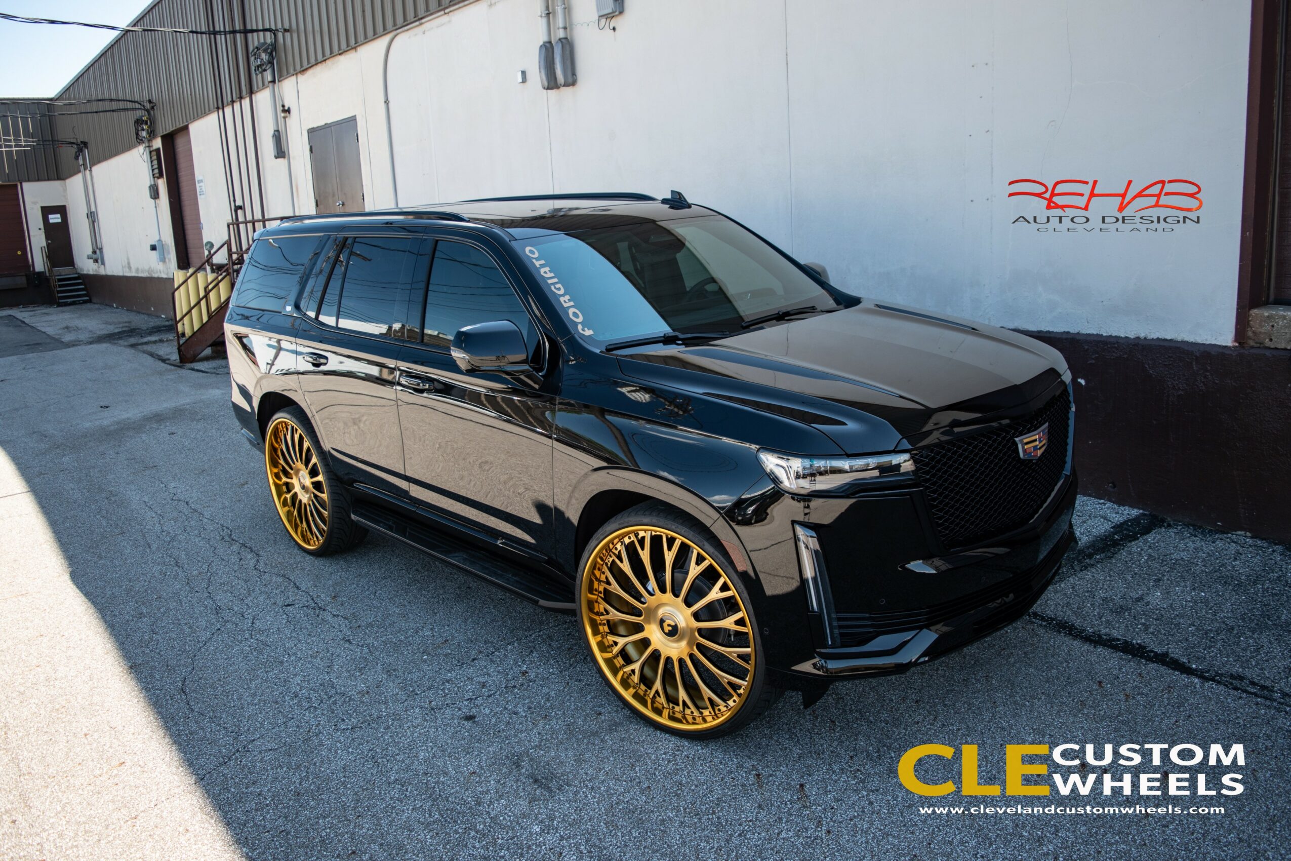 Black SUV with gold rims parked on street next to a white wall with red and black text.