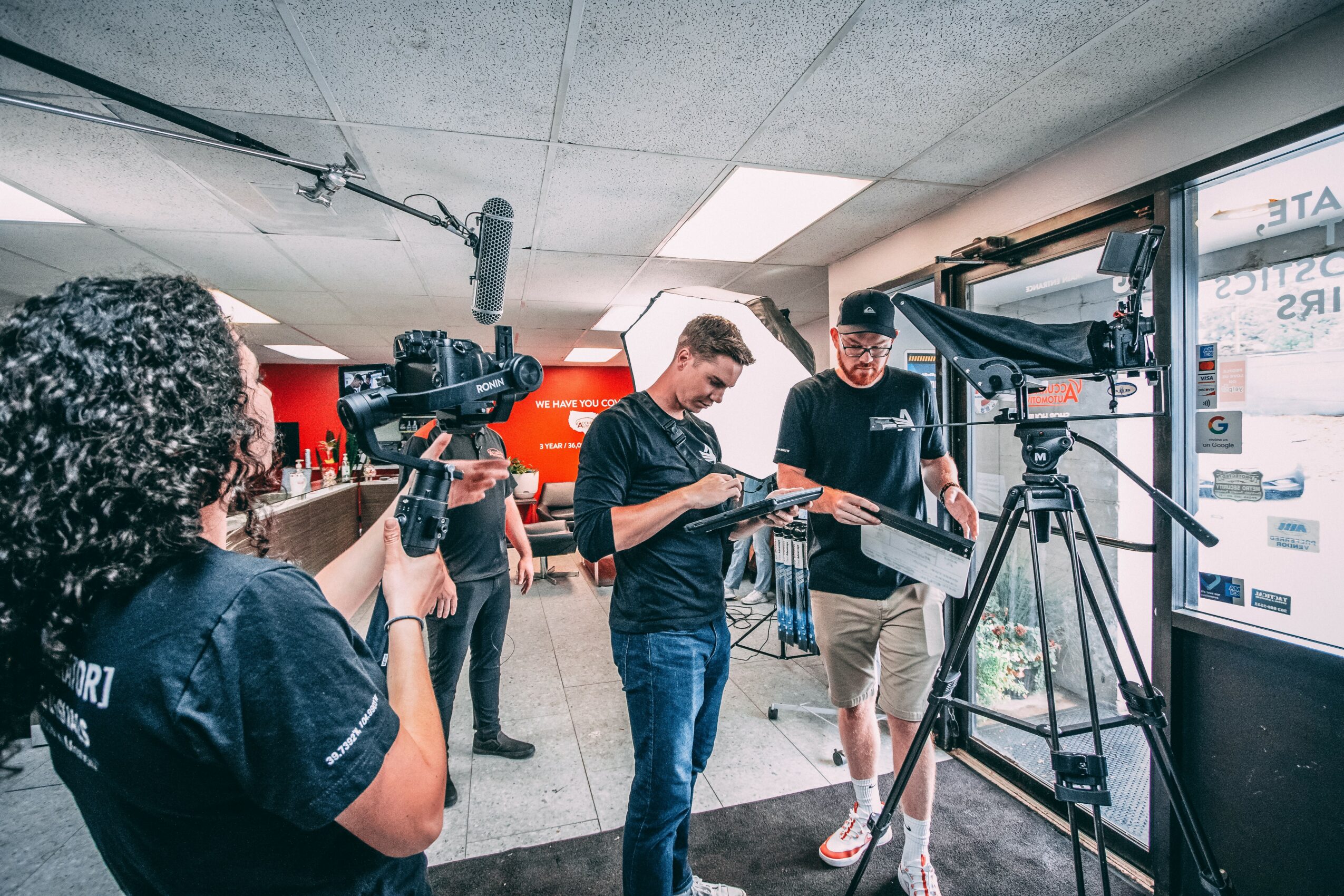 Group of people in a store, one person filming with a camera, others interacting near a large screen.