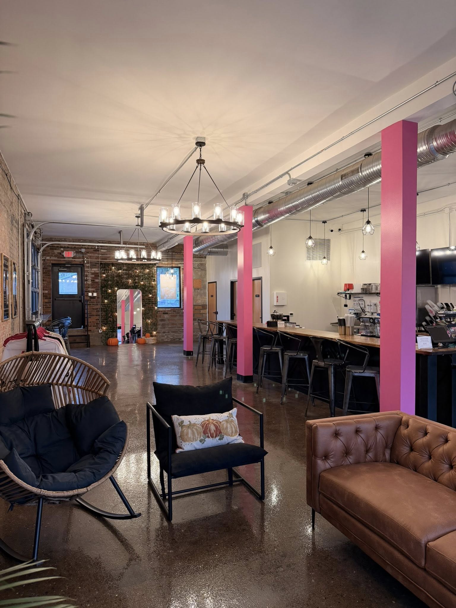 Interior of a cafe with seating, pink columns, and a bar area with hanging lights.