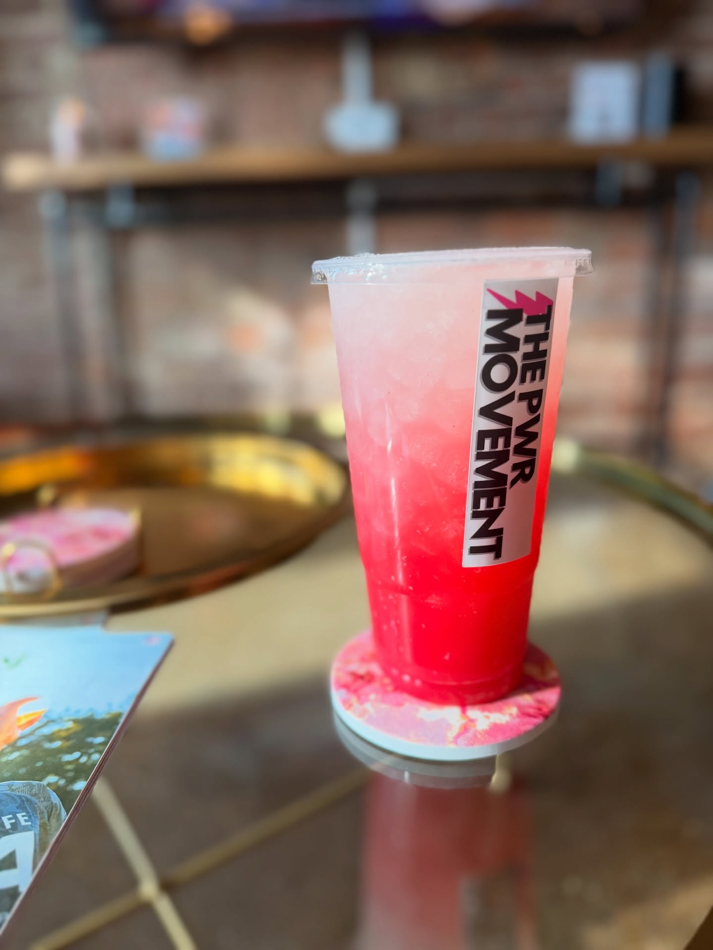 Pink and red layered drink in a clear cup with a straw, on a glass table.