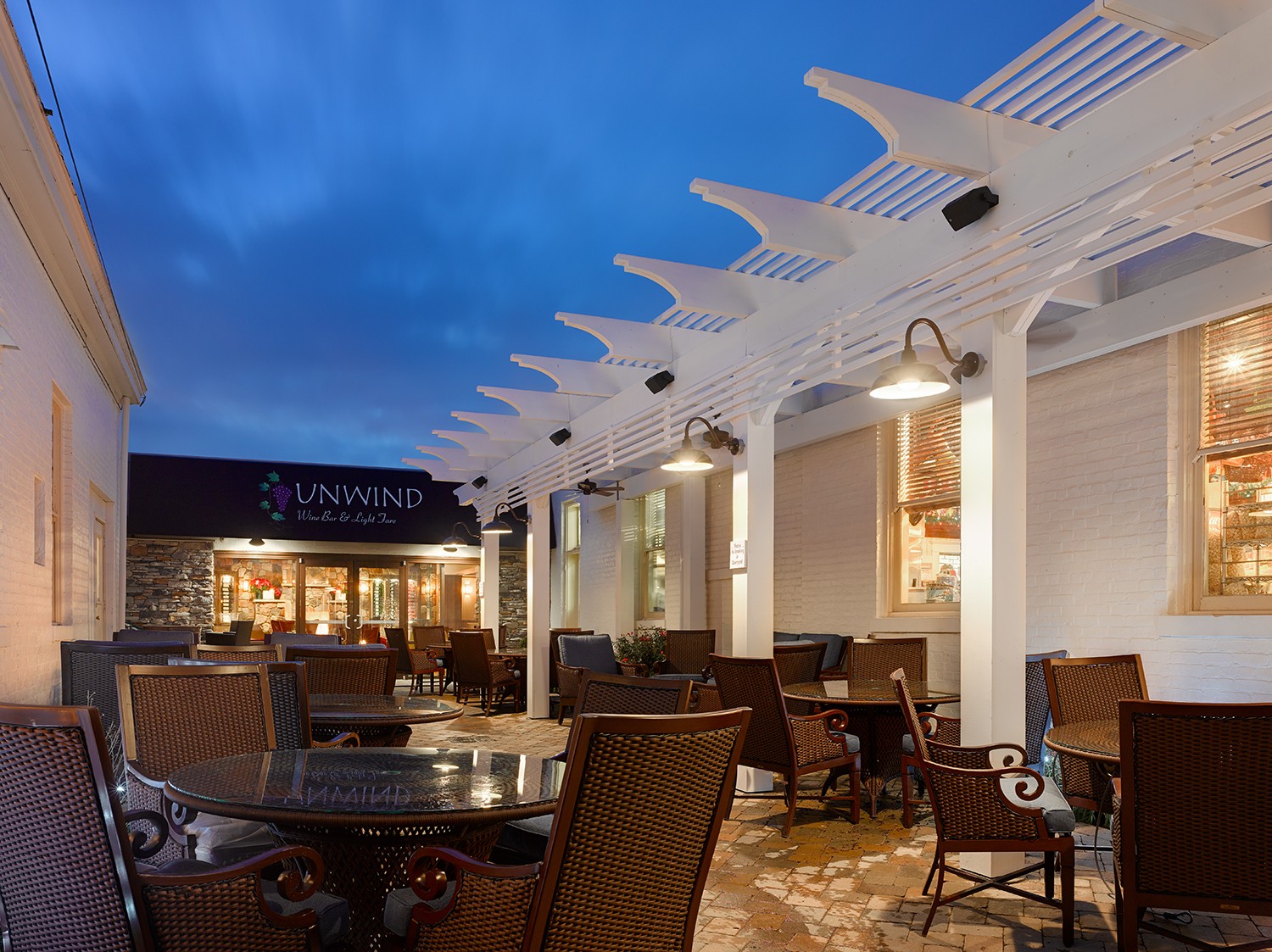 Outdoor seating area with tables and chairs under a white pergola against a evening sky.