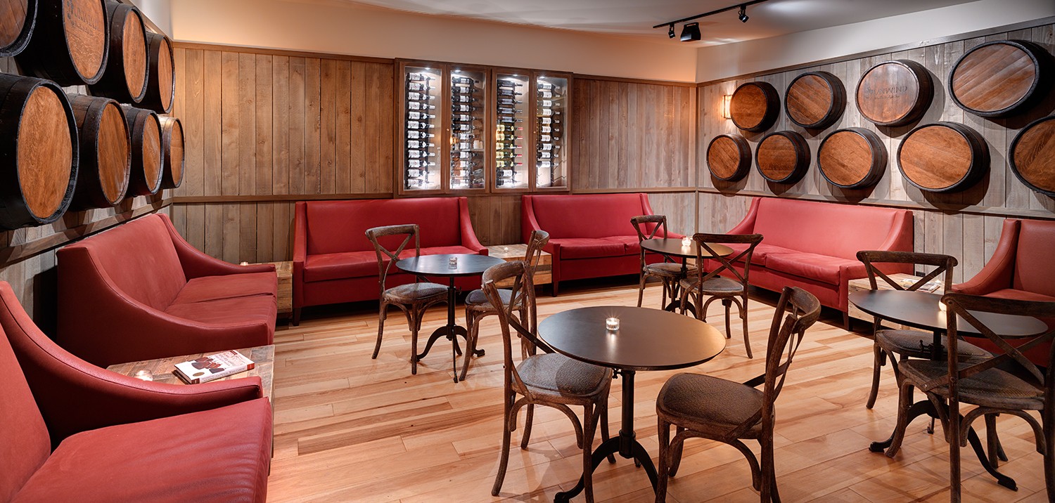 Room with red sofas, wooden tables, wine barrels on walls, and wooden flooring.
