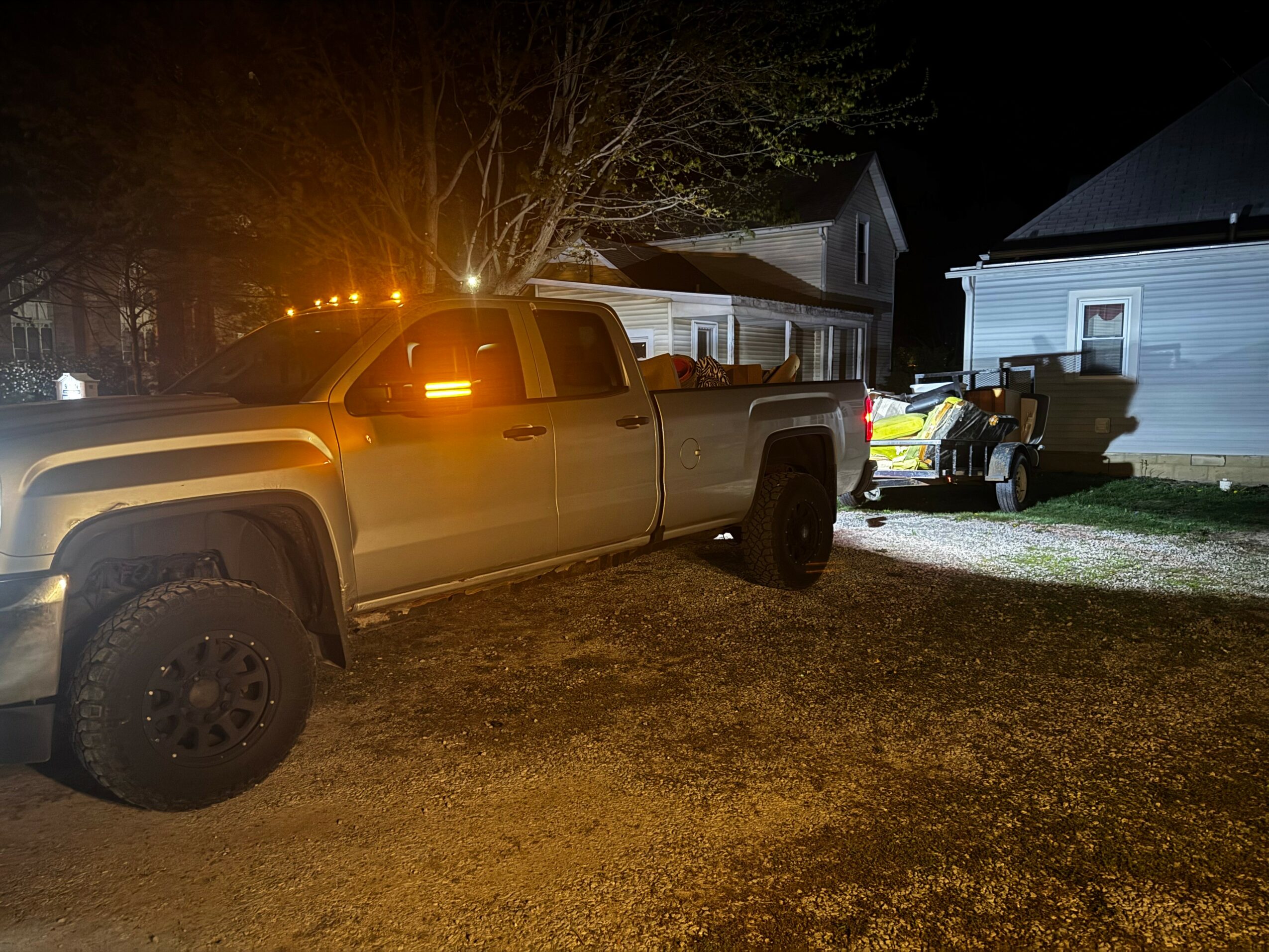 Night scene with a large pickup truck towing a small trailer near houses, illuminated by streetlights.