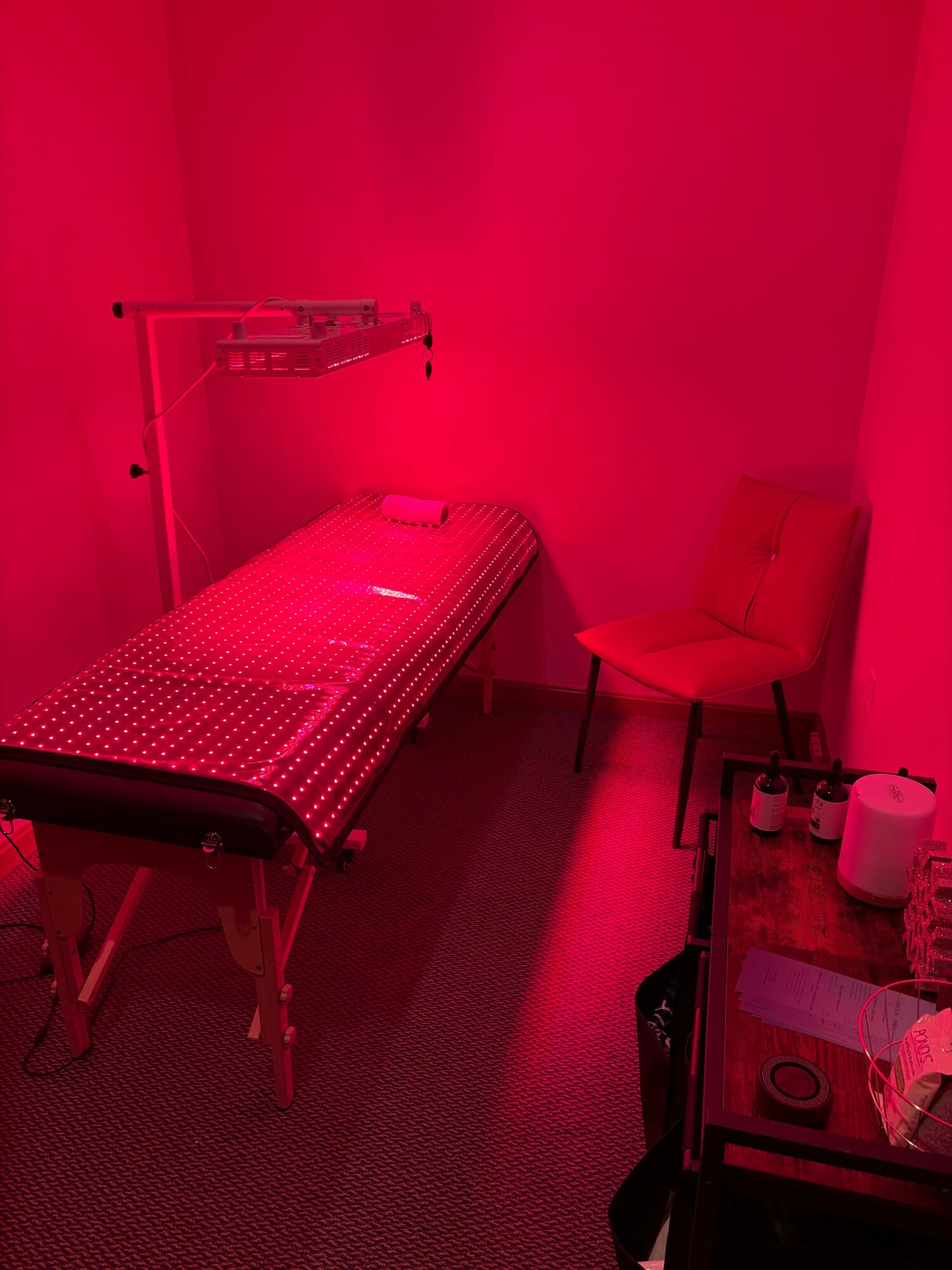 Room with a bed, chair, and a table with cups illuminated by red light.