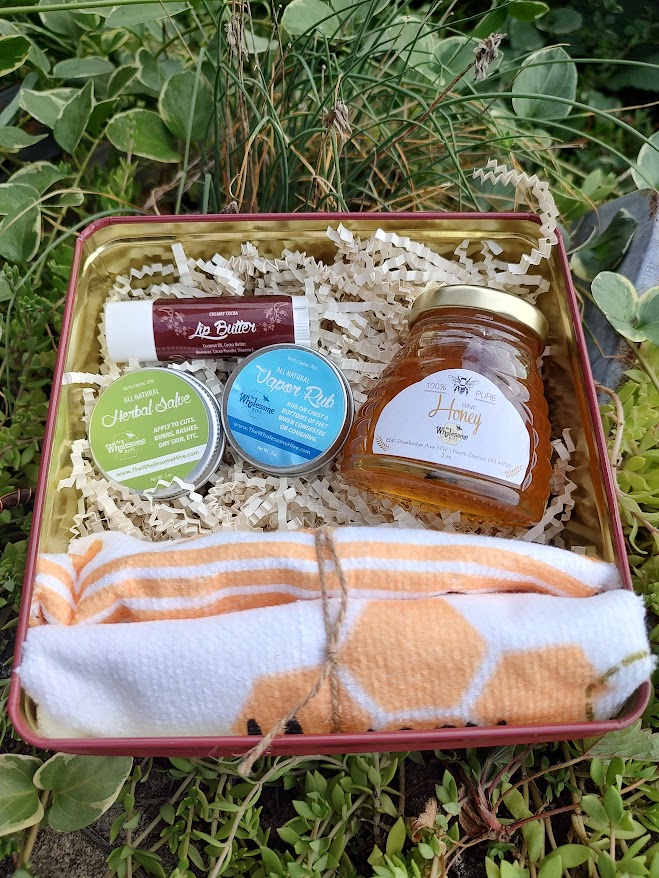 Gift box with jars, containers, and a towel on green grass background.