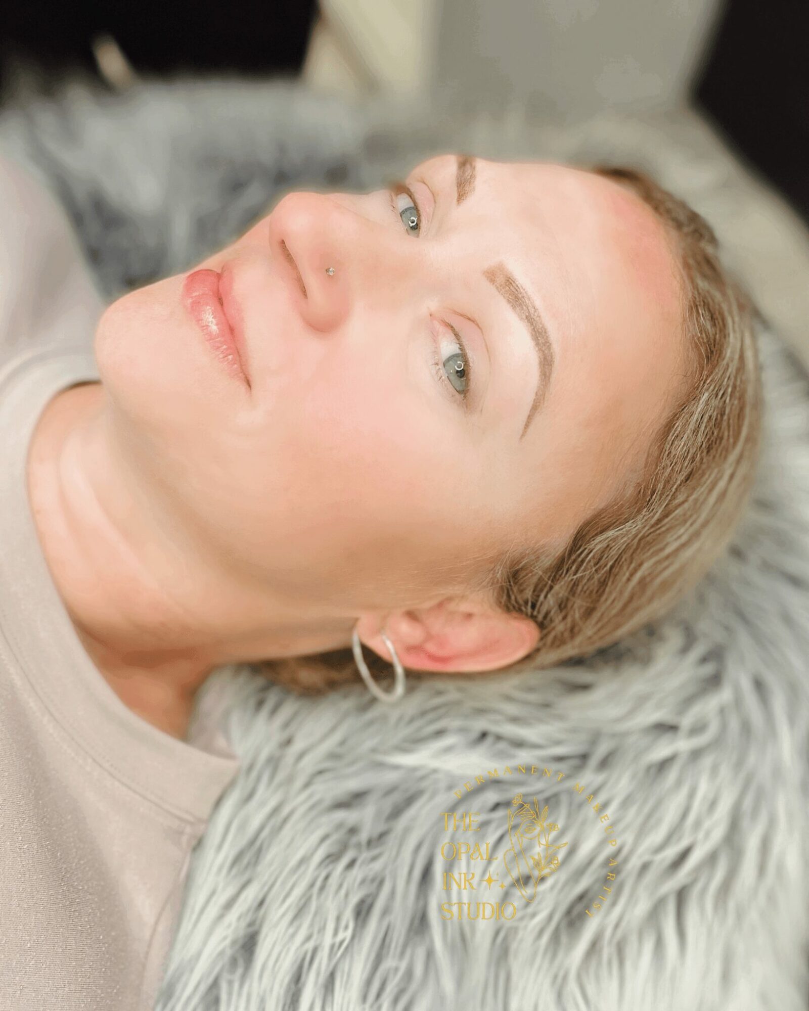 Woman with blonde hair lying on a furry surface, looking upward with a slight smile, wearing hoop earrings.