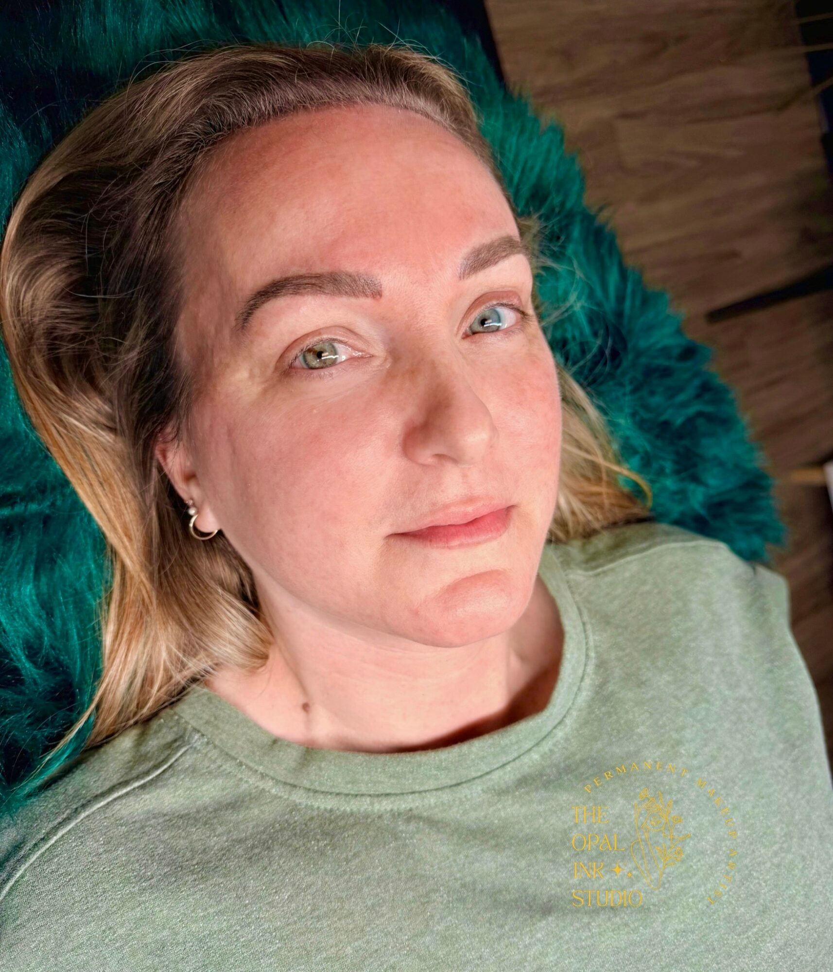 Woman with light brown hair lying on a teal blanket, wearing a light green shirt, looking at the camera.