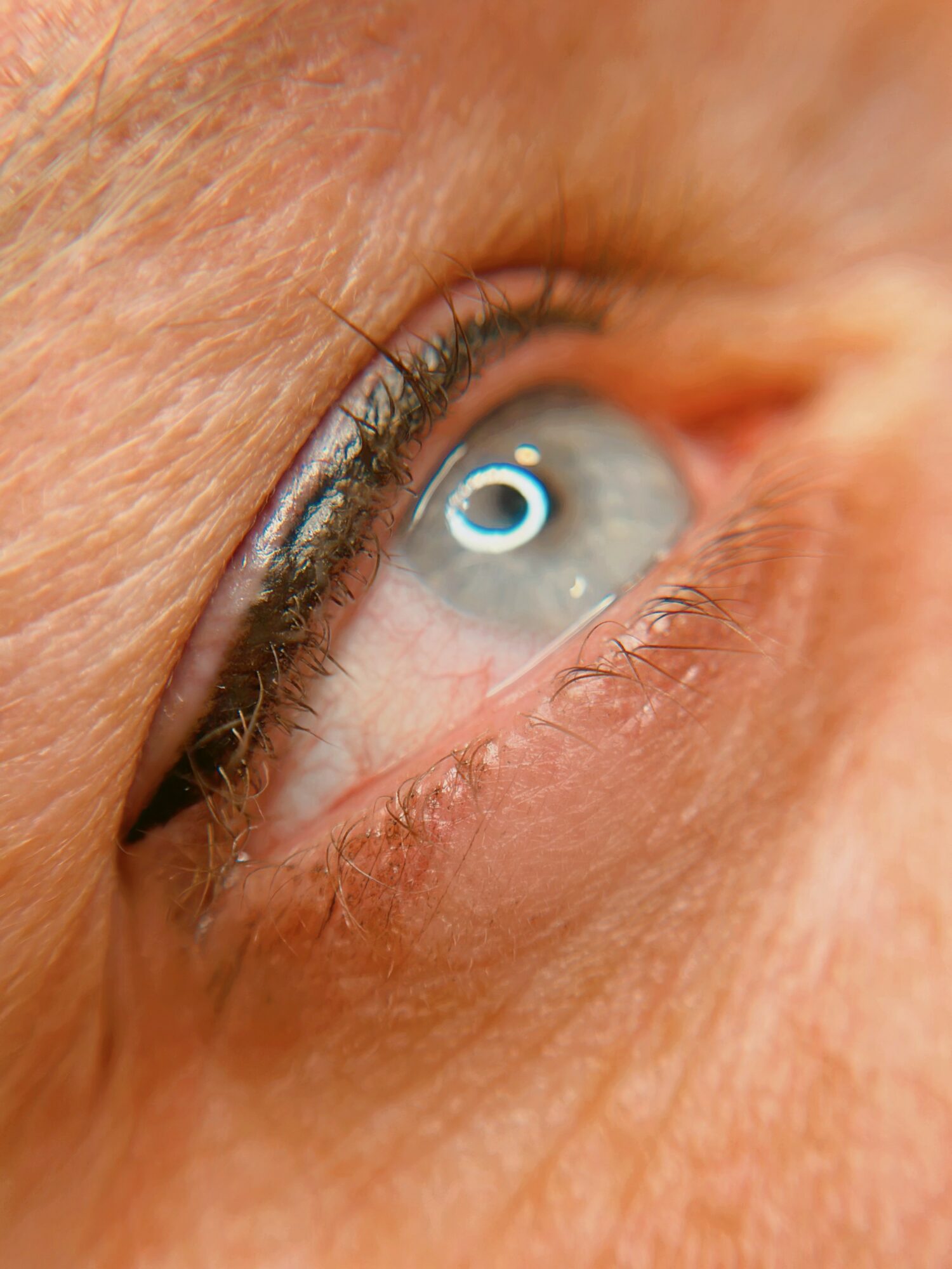 Close-up of a human eye with blue iris and visible eyelashes, surrounded by skin texture.