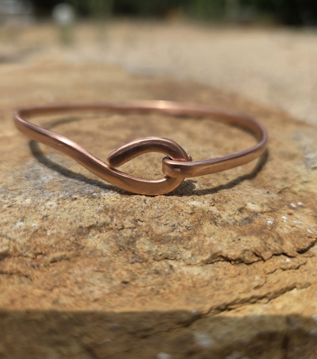 Copper bracelet with a hook design resting on a textured stone surface outdoors.