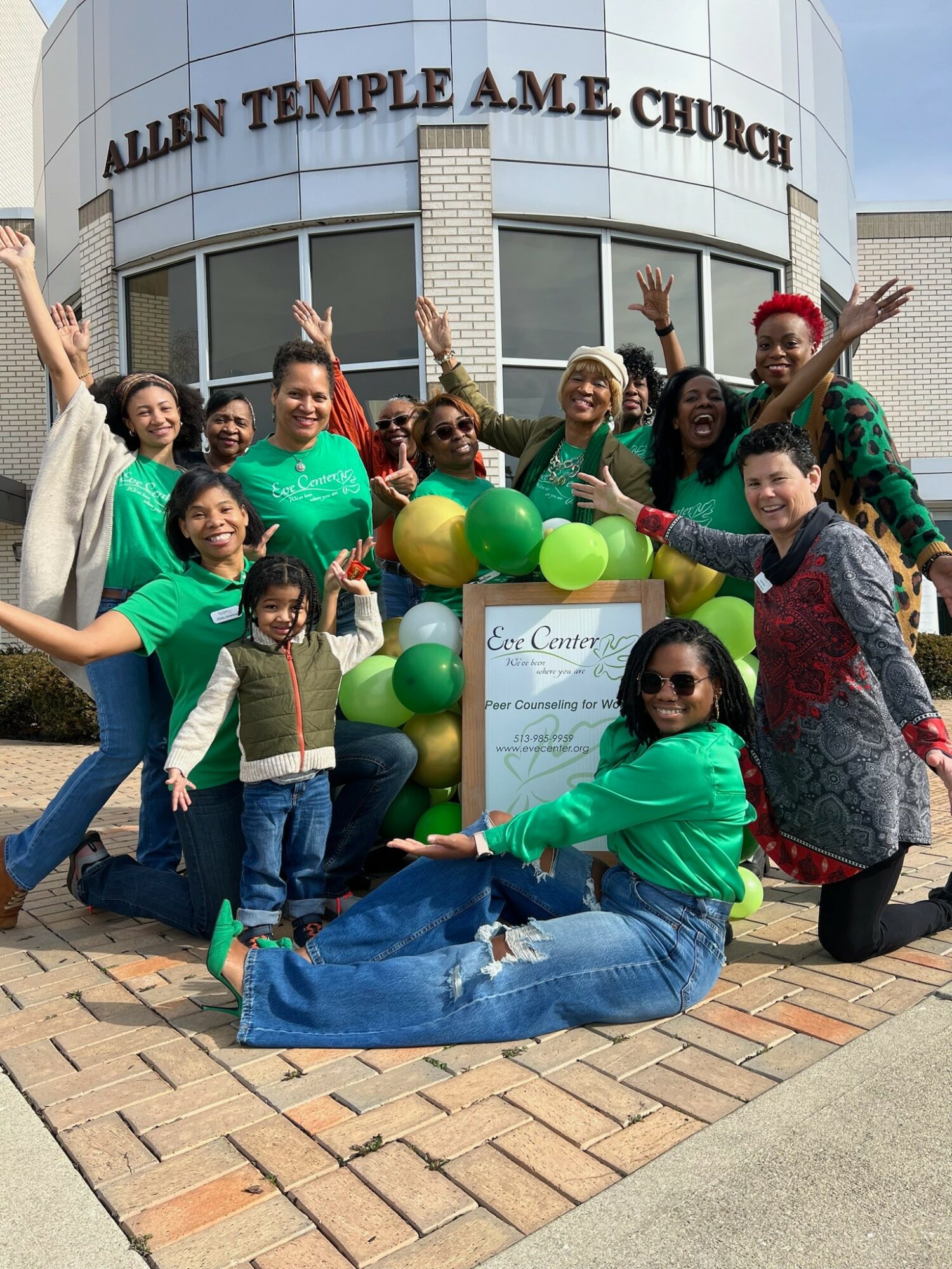 Group of diverse women and children smiling outside Allen Temple A.M.E. Church with balloons and a sign.