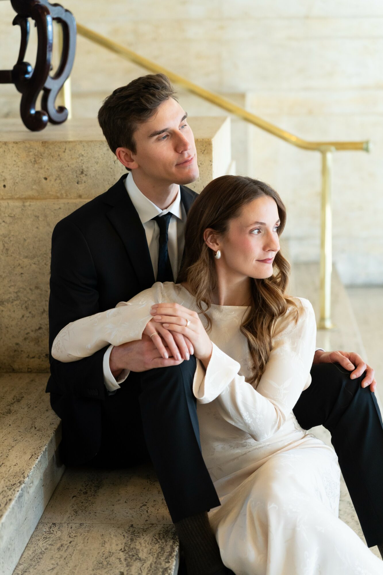 A man and woman sitting on stairs, holding hands, looking thoughtfully into the distance.