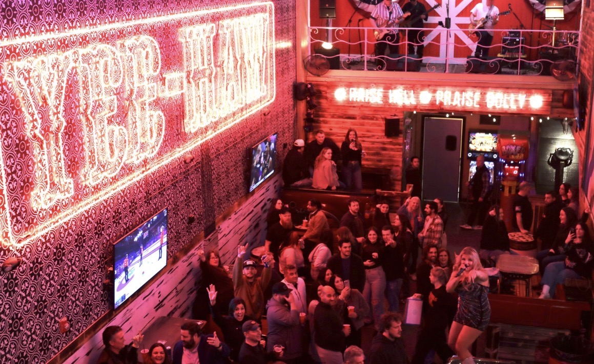 Crowd of people inside a lively bar with neon signs and British-themed decorations.