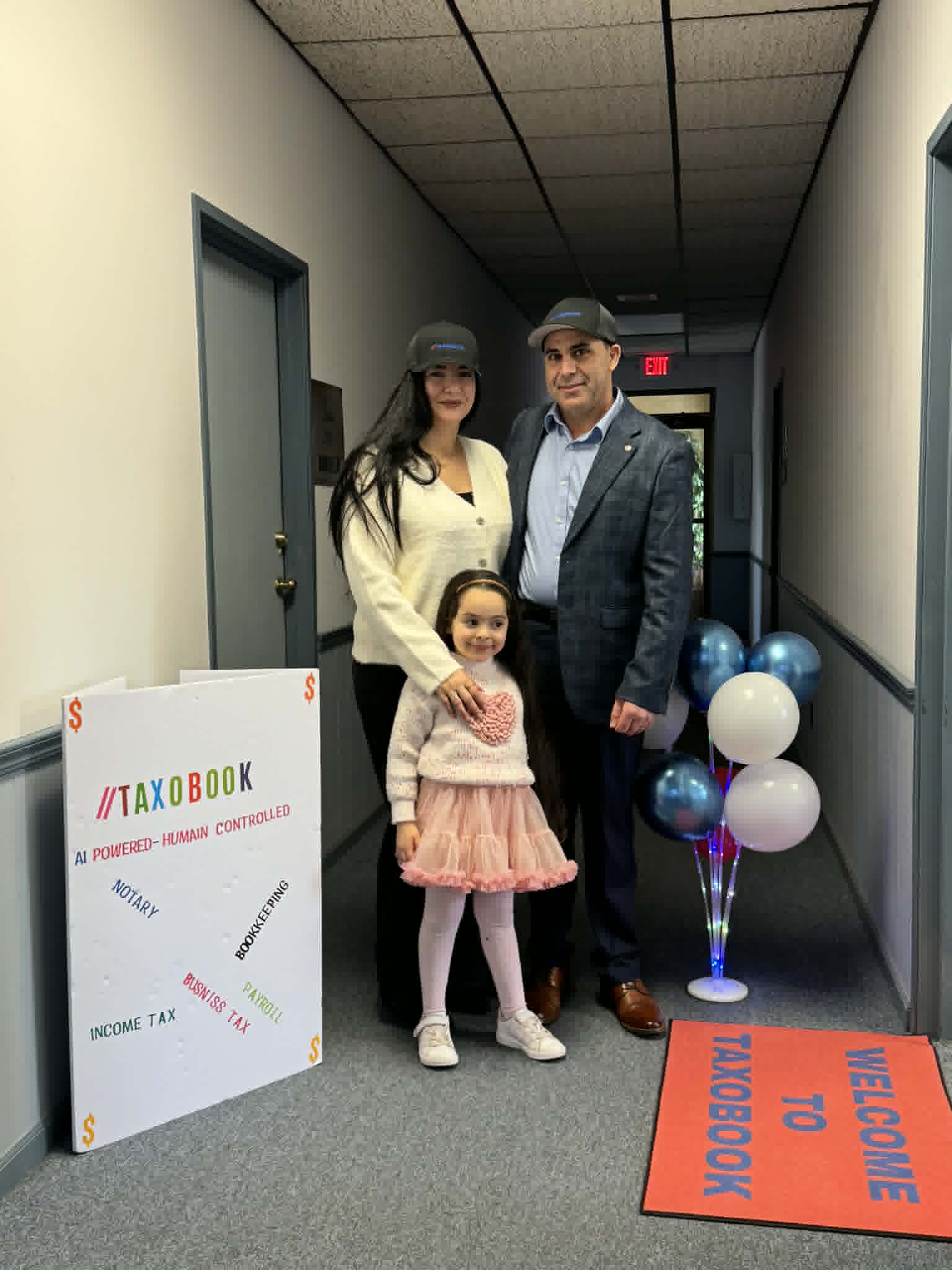 Three people, a man, a woman, and a girl, standing in a hallway with balloons and a welcome sign.