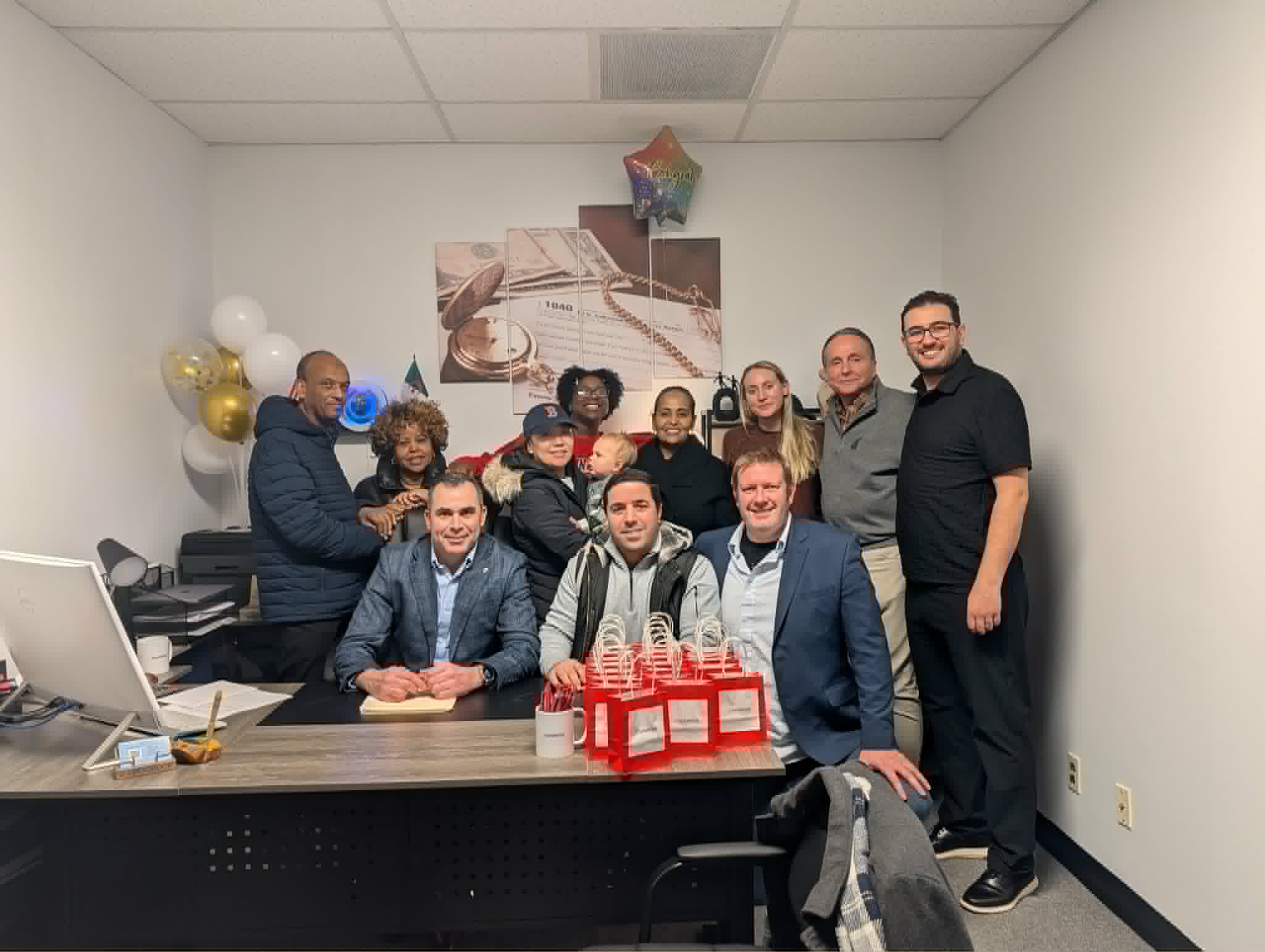 Group of ten people gathered around a desk in a room with balloons and a star-shaped decoration.
