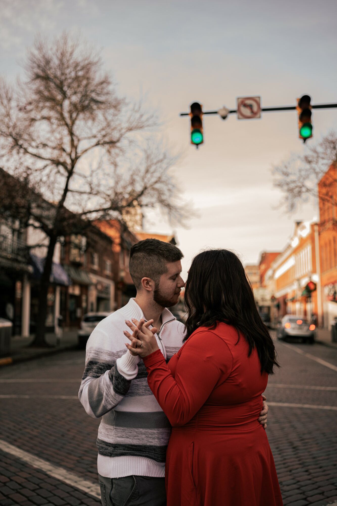 Couple holding hands and looking at each other on a city street with traffic lights overhead.