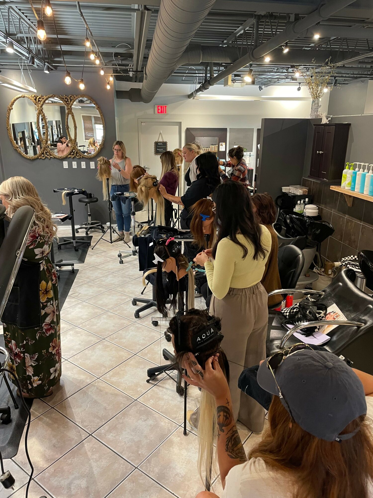 People in a hair salon with mirrors, chairs, and hair styling tools, some waiting and others getting haircuts.