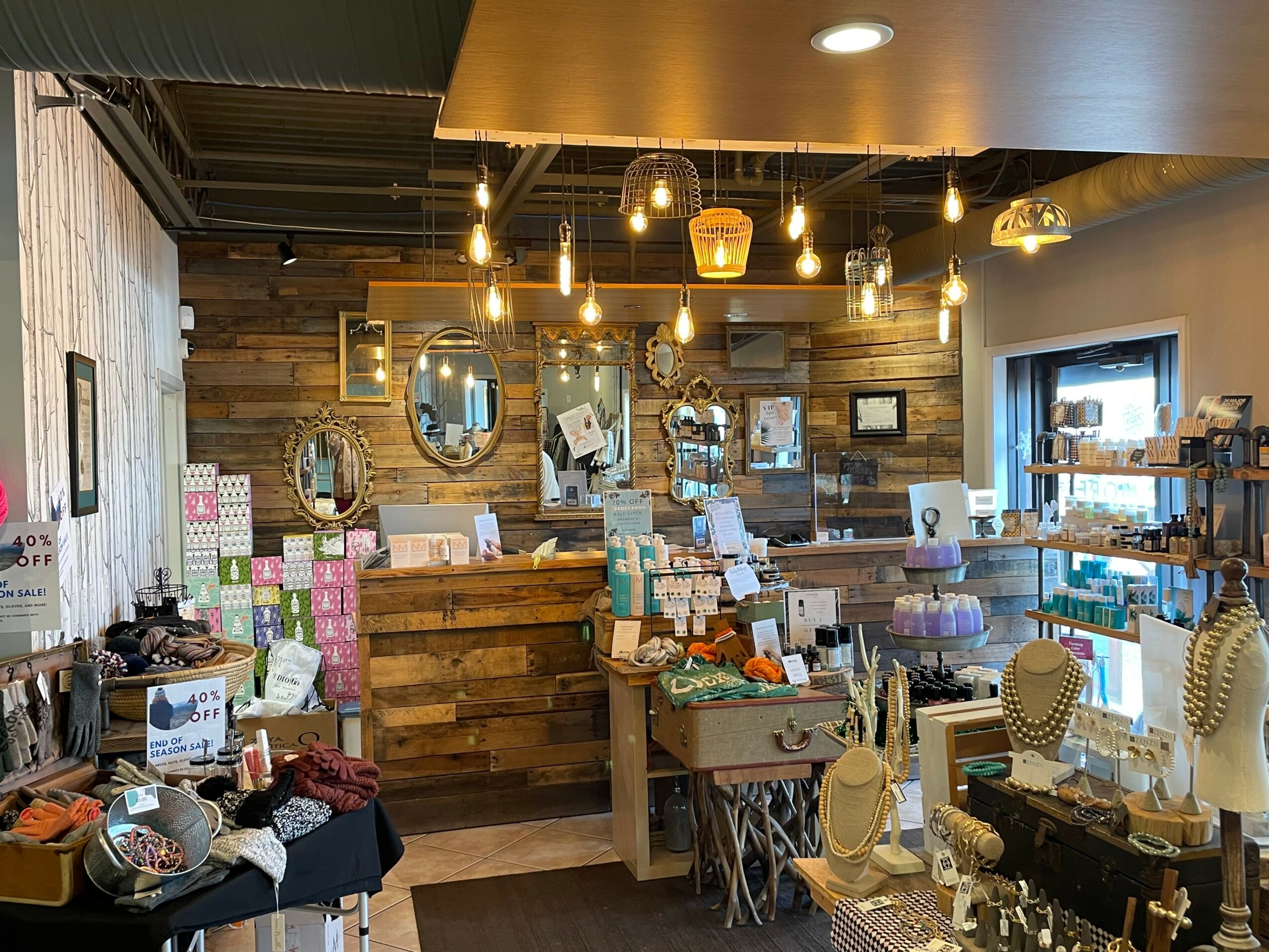 Interior of a boutique shop with wooden walls, hanging lights, mirrors, and display tables with accessories and jewelry.