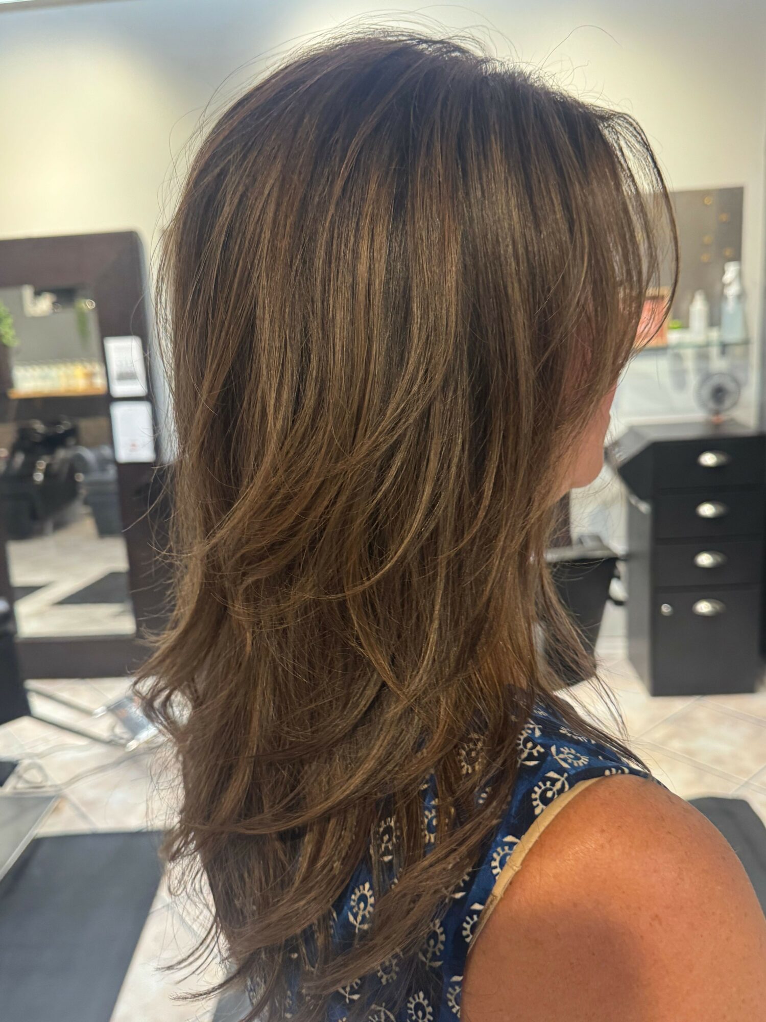 Side view of a woman with long, wavy brown hair in a salon setting.