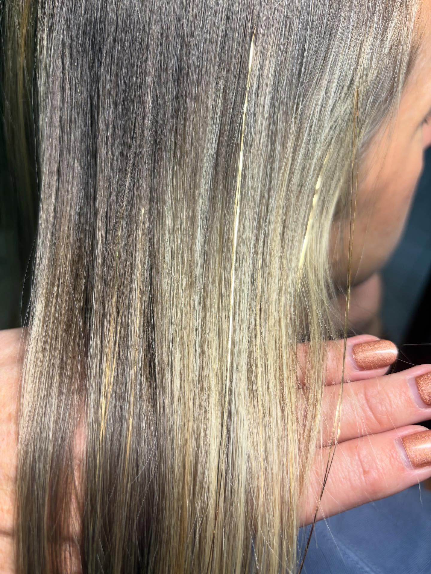 Close-up of straight, blonde hair with varying shades and highlights, held by a person's hand.