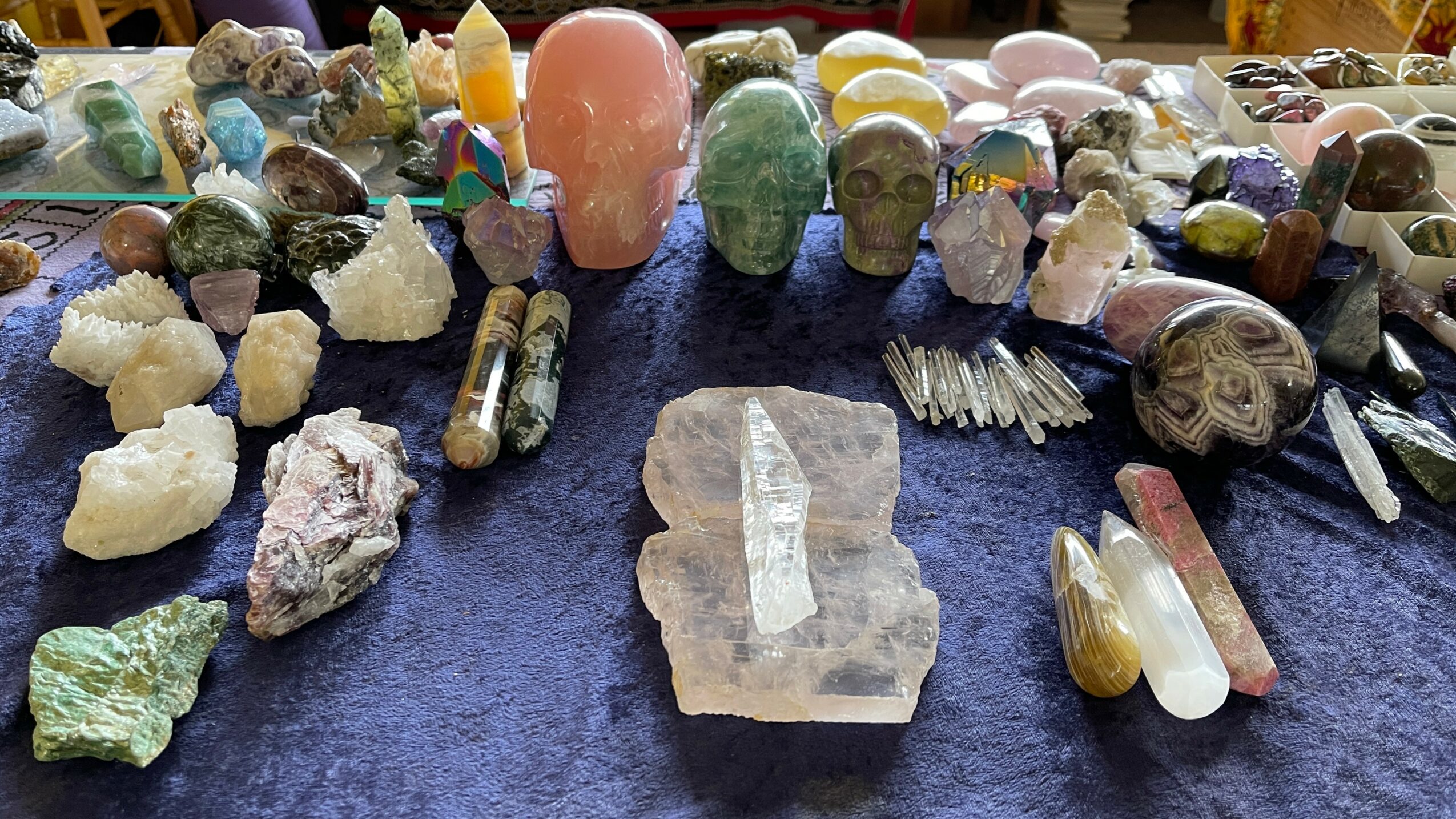Various crystals, minerals, and gemstones displayed on a dark surface, with some shaped into skulls and other objects.