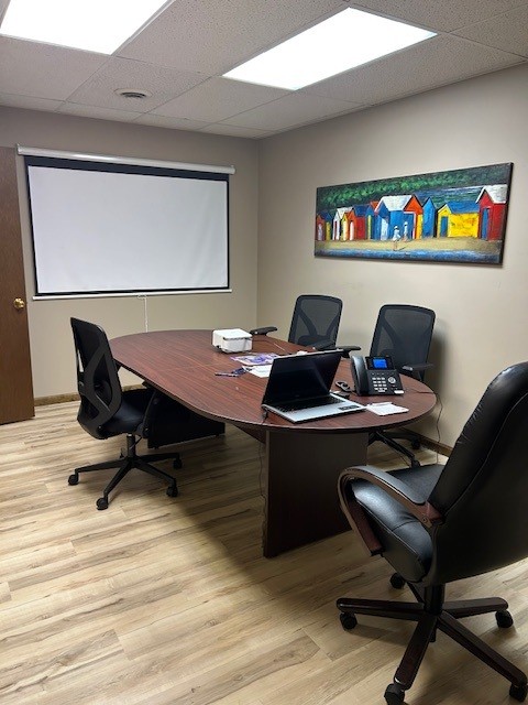 Conference room with a wooden table, four black chairs, a whiteboard, and a colorful painting on the wall.