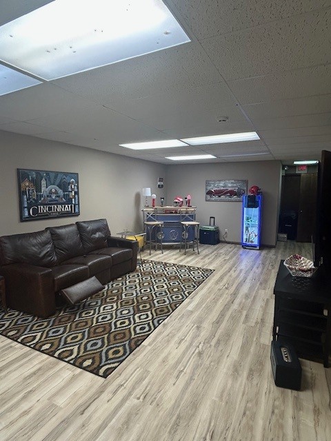Office lounge with a black sofa, patterned rug, vending machine, and a table with items, in a room with ceiling lights.