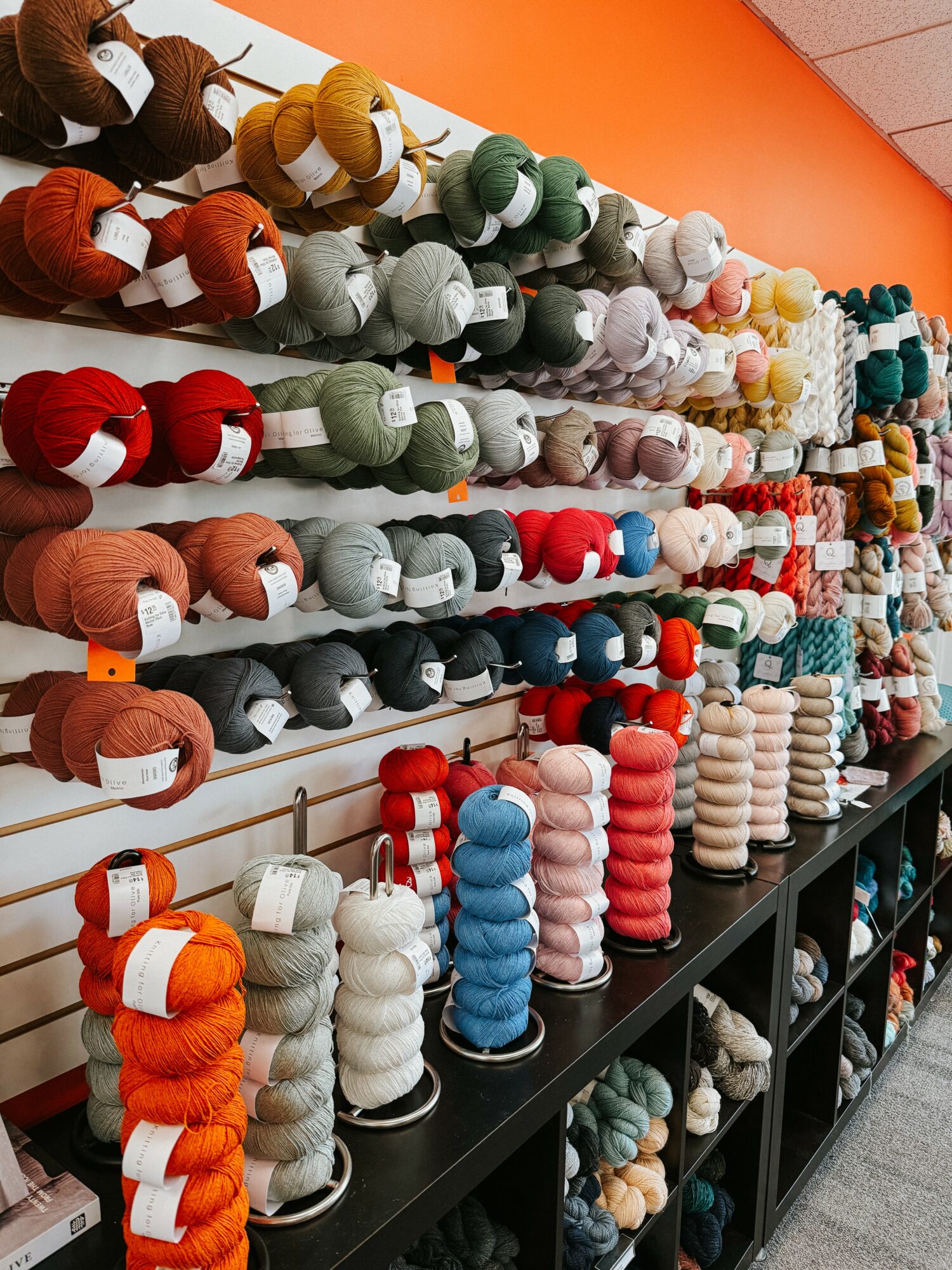 Display of colorful yarn skeins on shelves in a store, arranged by color and size.