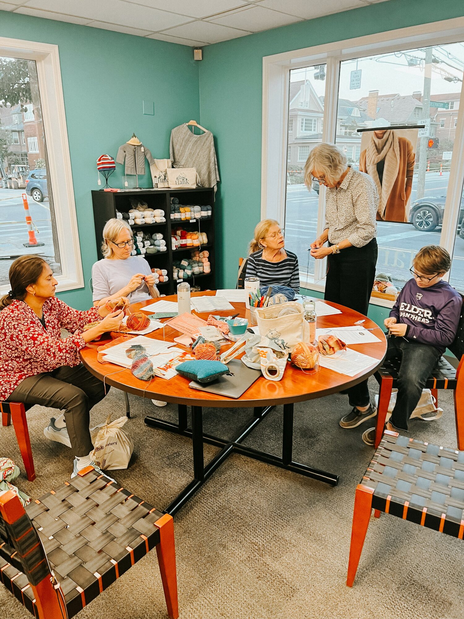 Group of children and an adult around a round table in a room with large windows, colorful walls, and craft supplies.