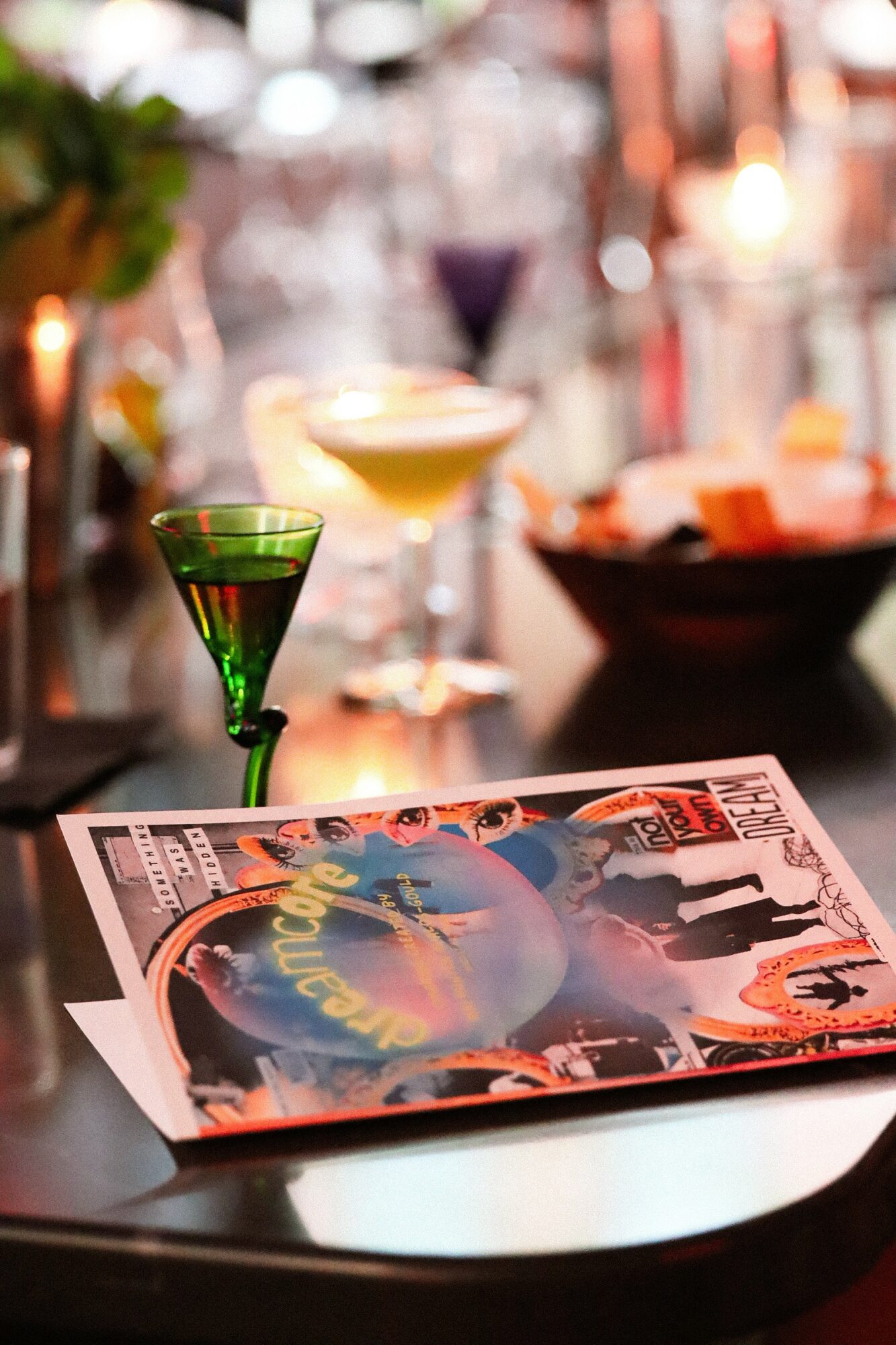 Cocktail glasses and a menu on a dark table with blurred bar background.