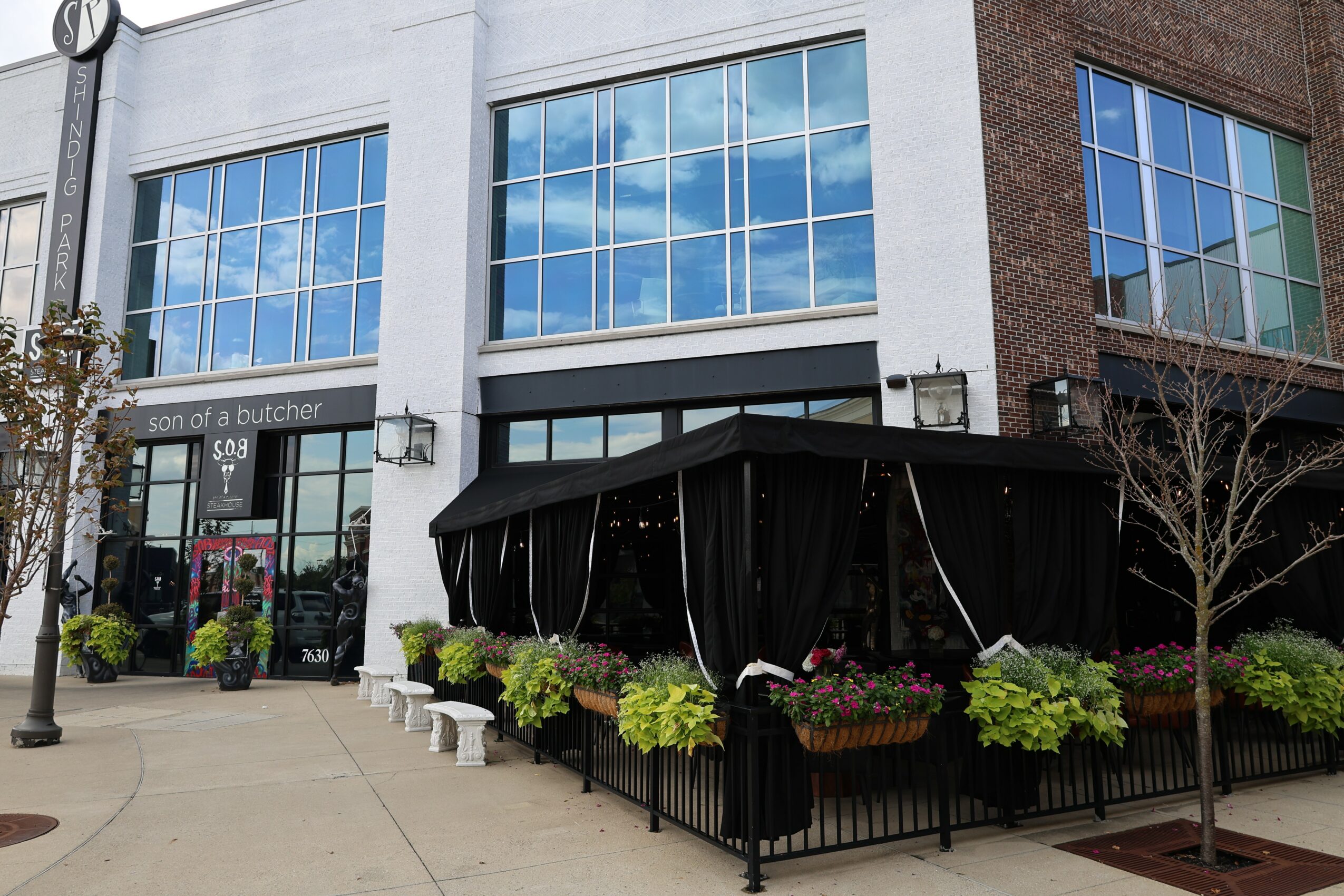 Building with large glass windows and a black canopy covering an outdoor seating area with plants.