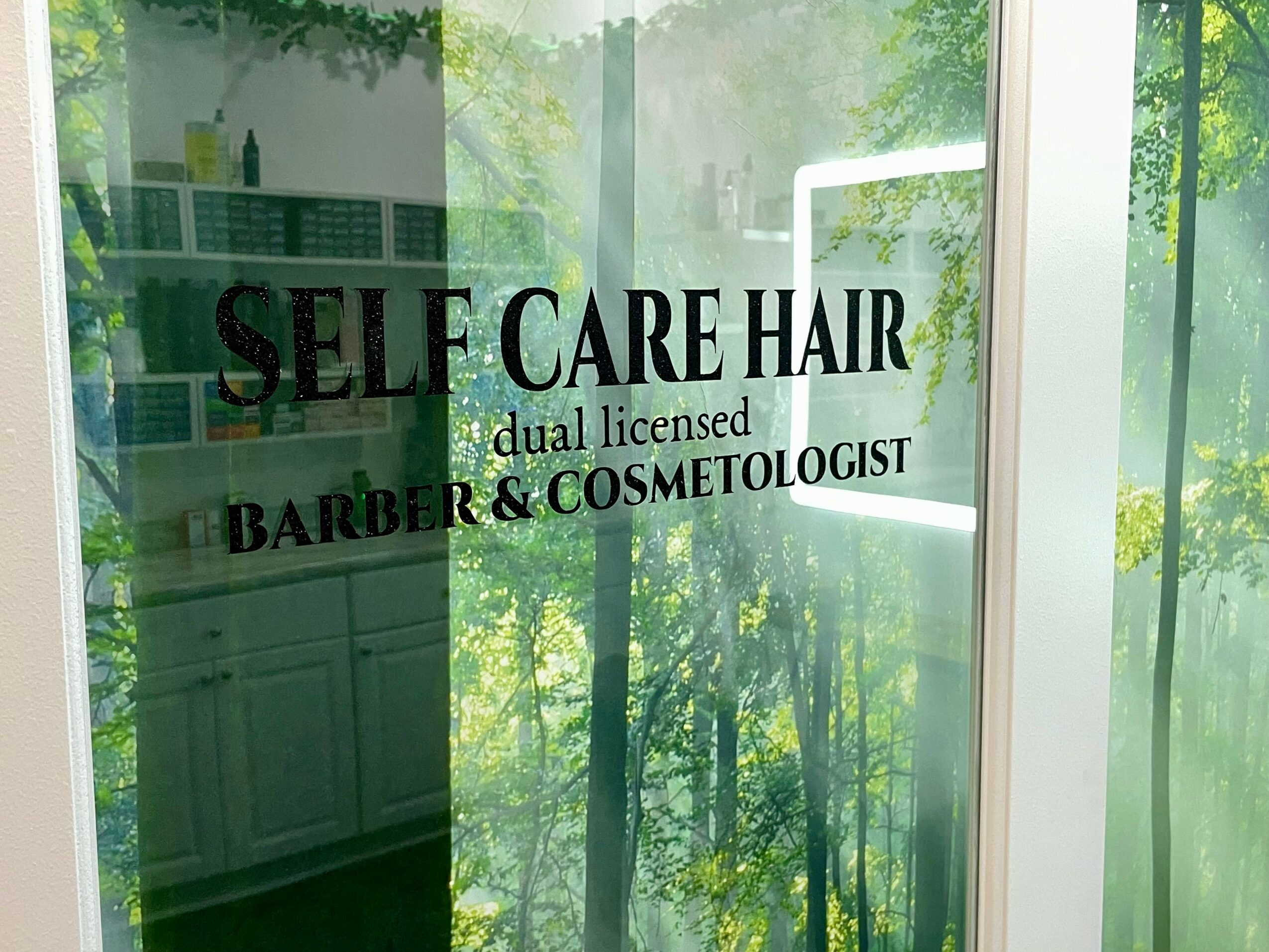 Sign for a hair salon with trees and greenery reflected in the window.