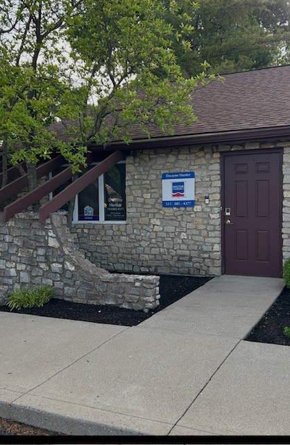 Stone building with purple door, window, and sign, surrounded by trees and a concrete walkway.