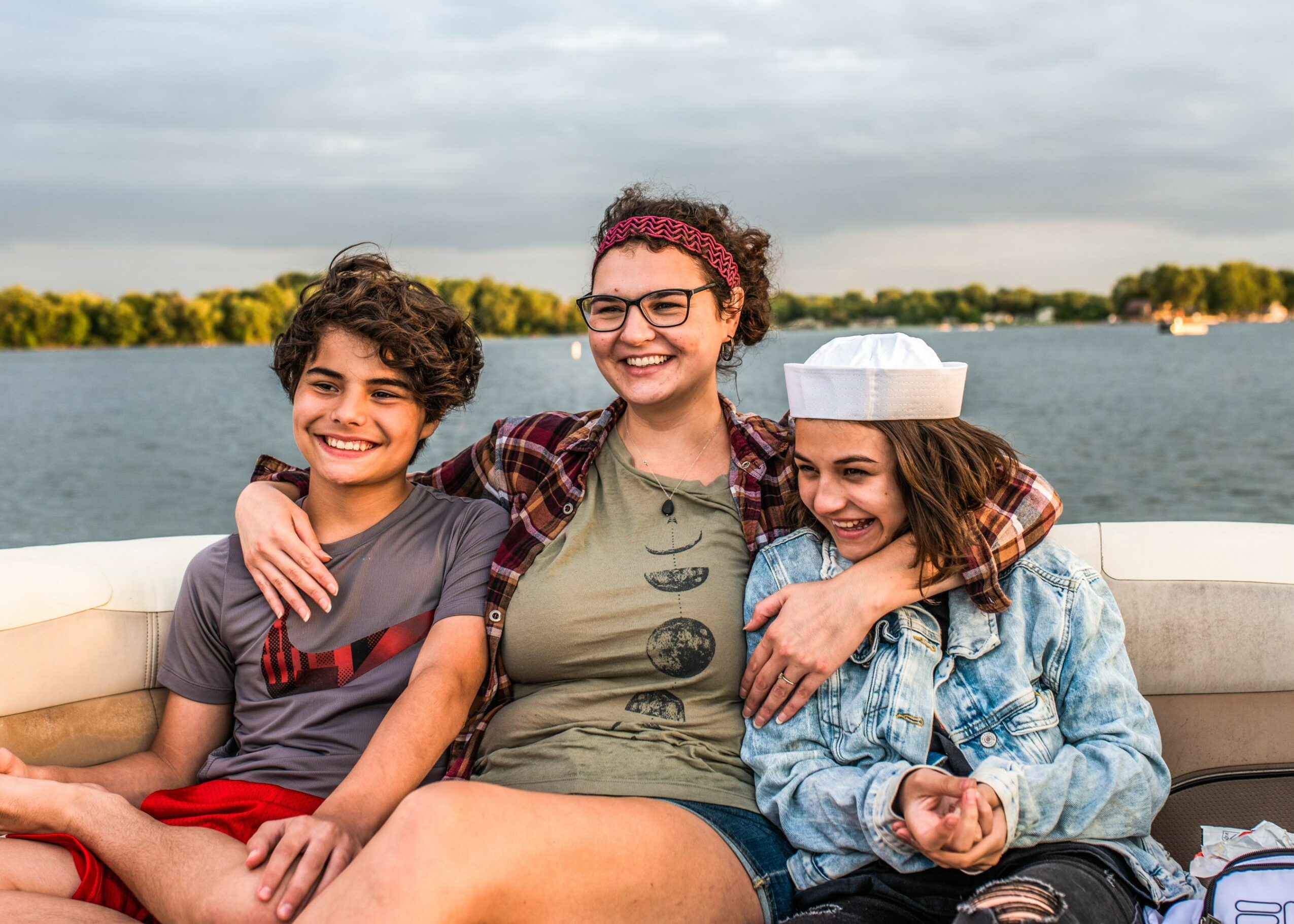 Three people sitting on a boat with water and trees in the background, smiling and enjoying each other's company.